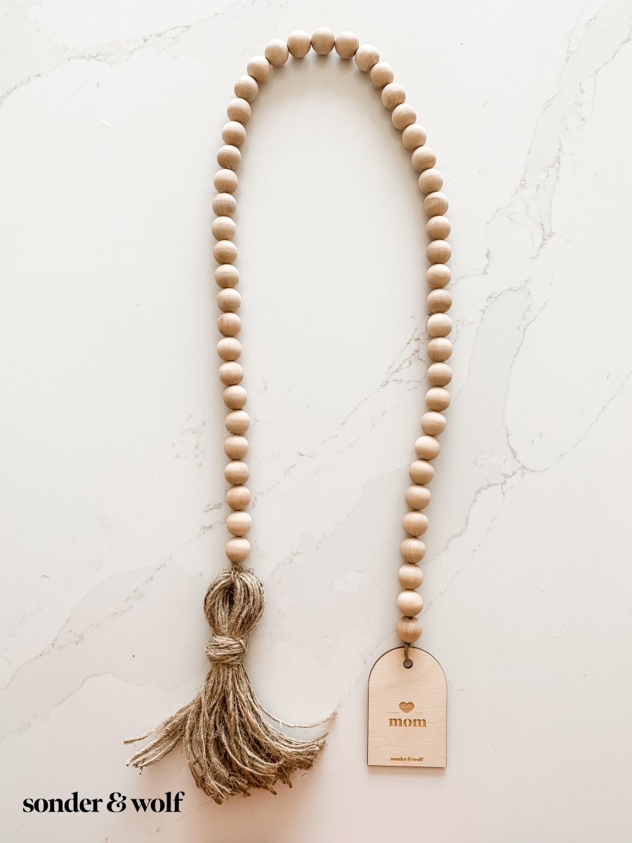 Mom Garland featuring light wood beads and a jute tassel, perfect for home decor.