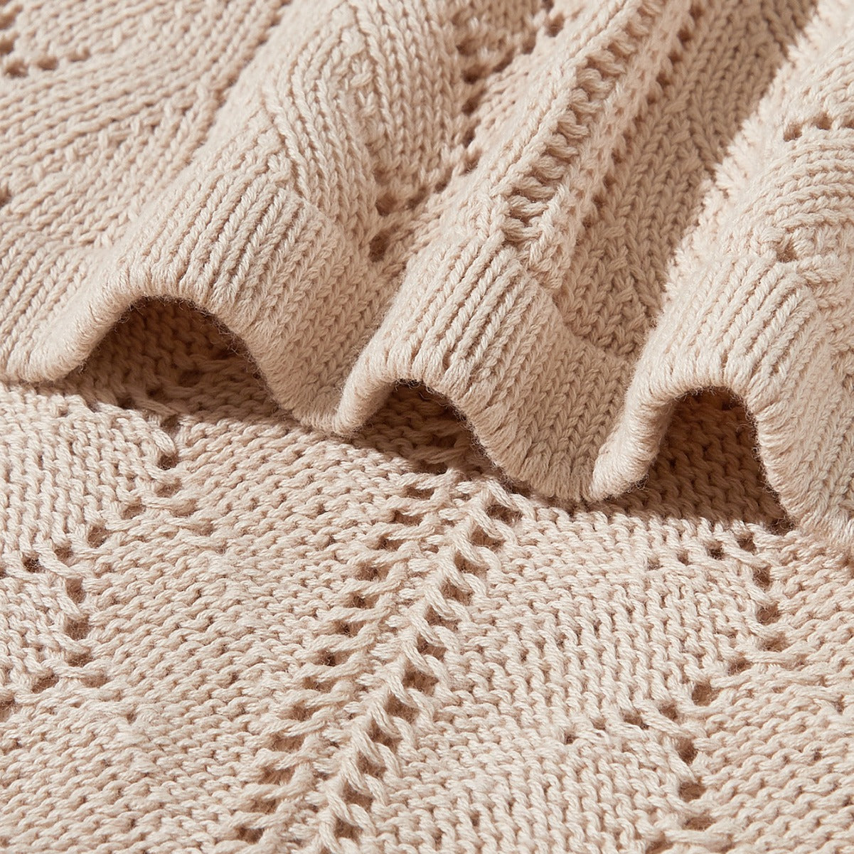 A cozy beige knitted baby blanket featuring a stylish hollow-out design, perfect for infants and toddlers.