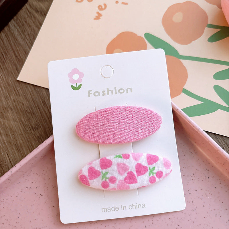 Two candy-colored oval cloth hair clips in pink and blue, featuring fun patterns, perfect for baby girls and young girls.