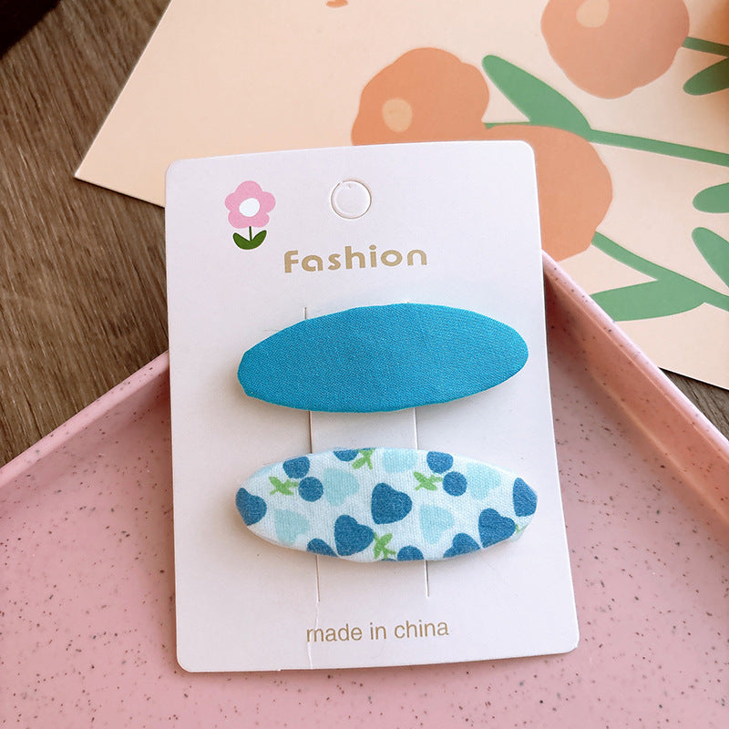 Two candy-colored oval cloth hair clips in pink and blue, featuring fun patterns, perfect for baby girls and young girls.