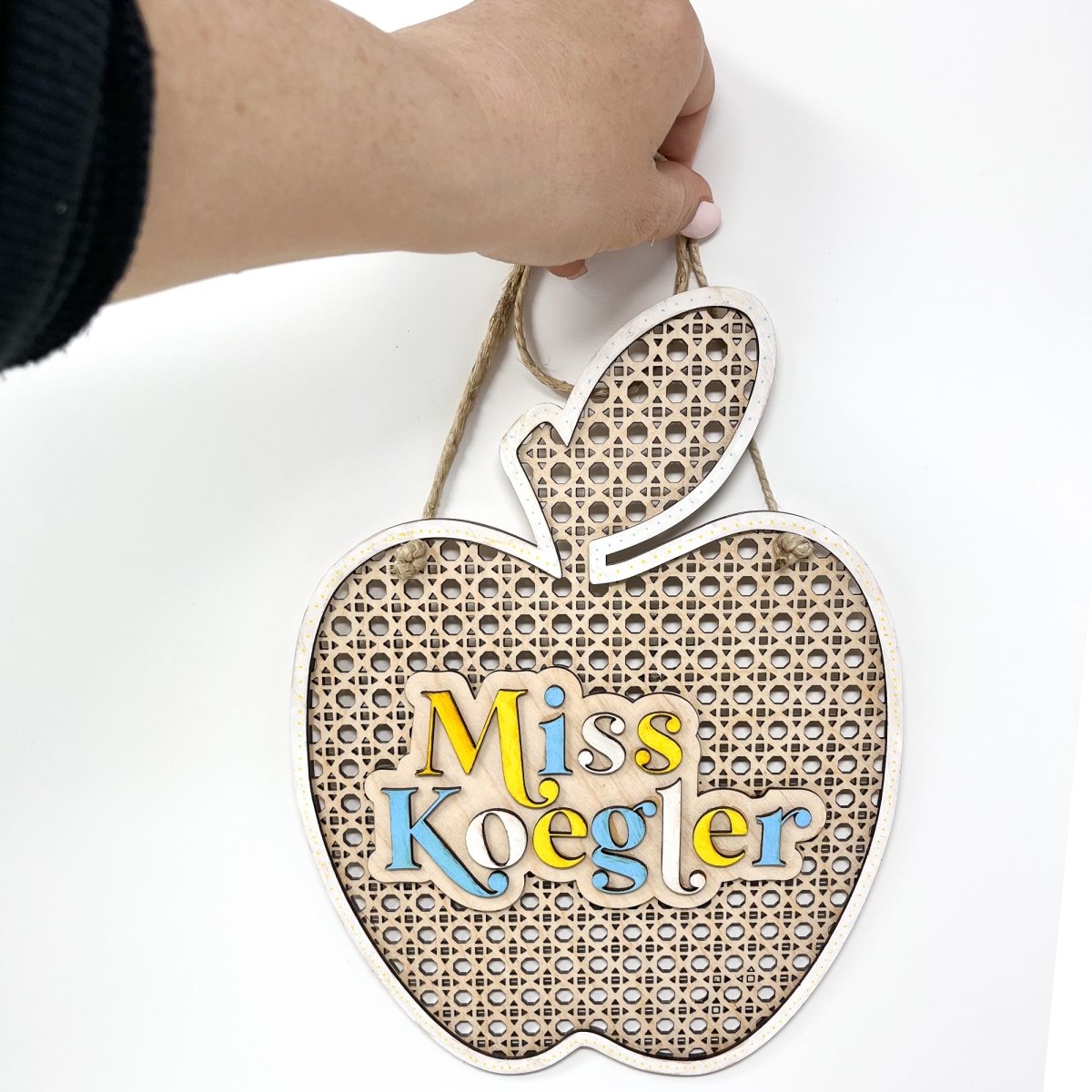 A personalized rattan apple sign for teachers, featuring raised lettering and colorful design, ready to hang with jute rope.