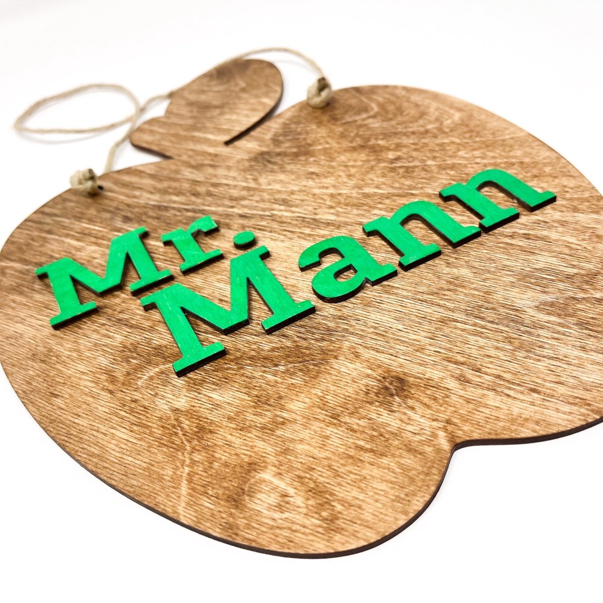 A personalized teacher apple sign made of natural wood, featuring raised lettering and colorful design, ready to hang with jute rope.