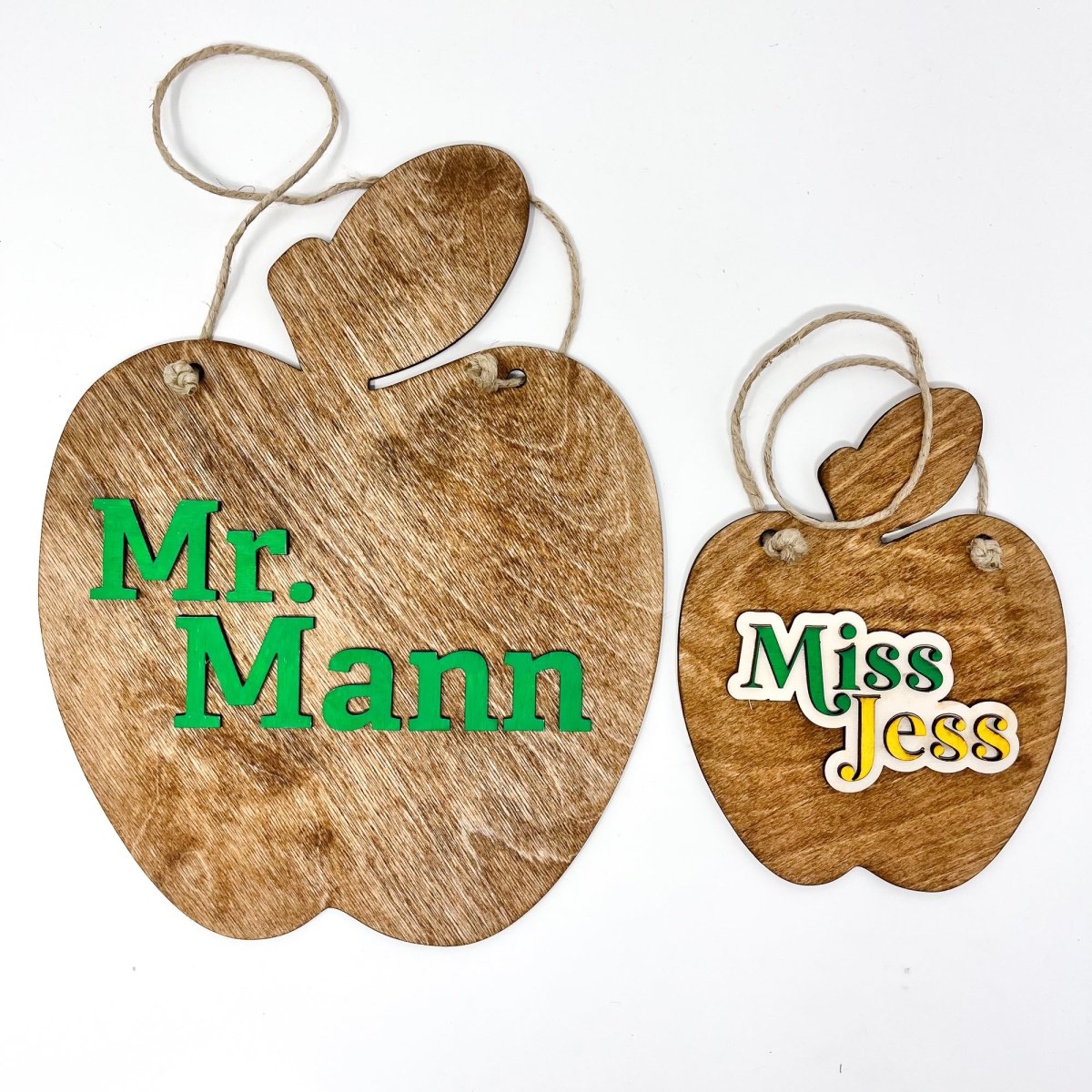 A personalized teacher apple sign made of natural wood, featuring raised lettering and colorful design, ready to hang with jute rope.