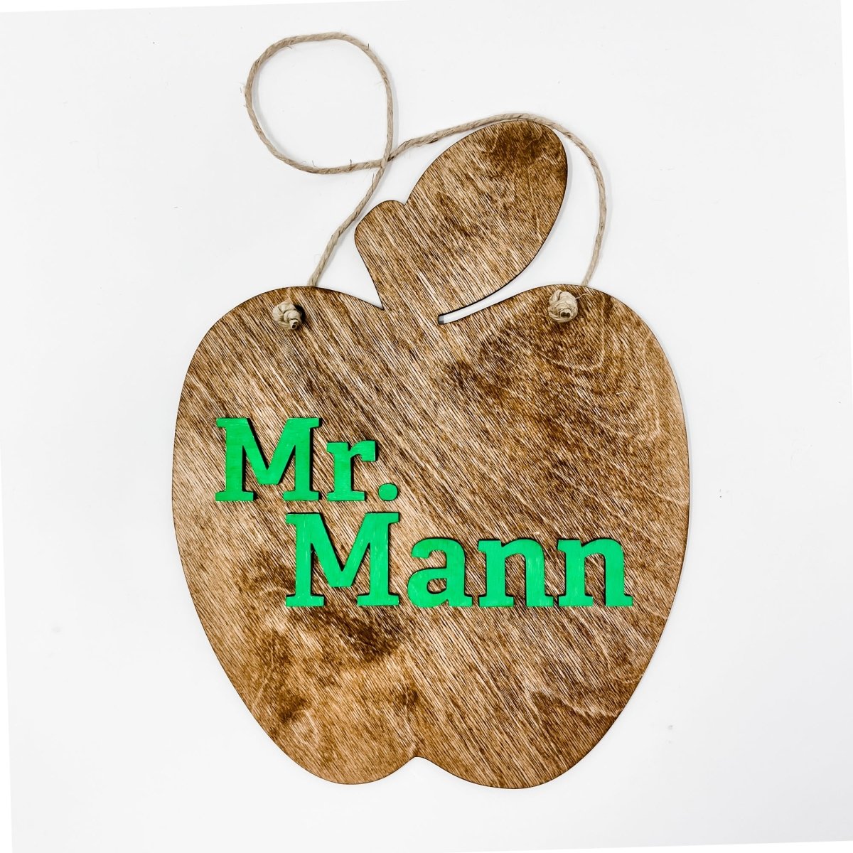 A personalized teacher apple sign made of natural wood, featuring raised lettering and colorful design, ready to hang with jute rope.