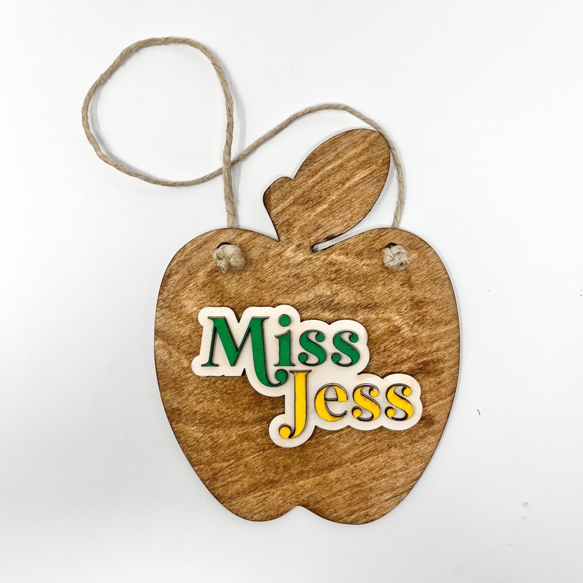 A personalized teacher apple sign made of natural wood, featuring raised lettering and colorful design, ready to hang with jute rope.