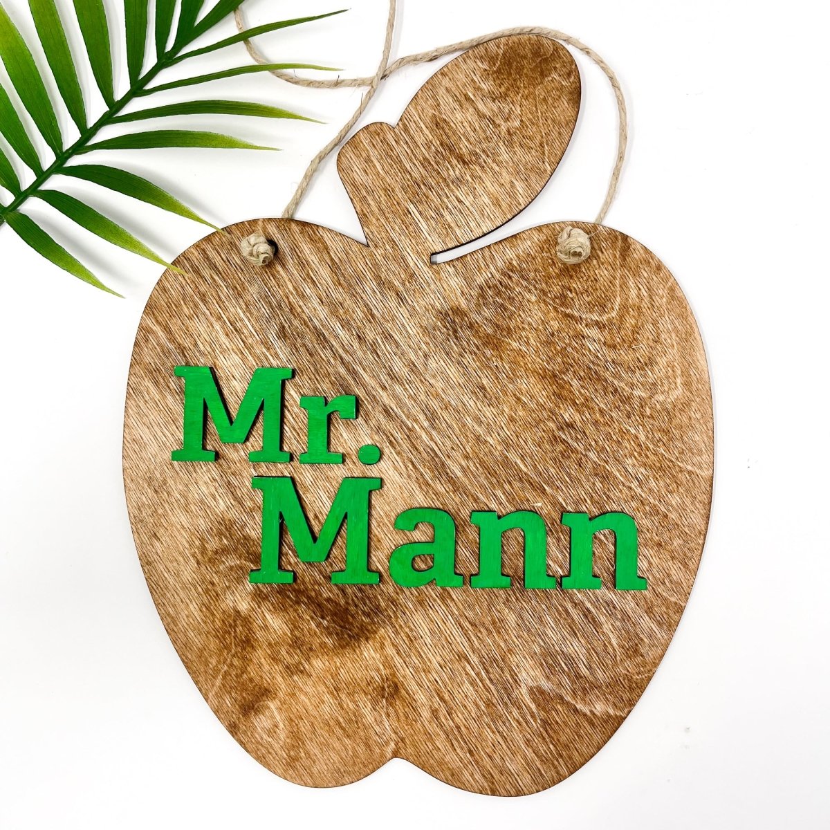 A personalized teacher apple sign made of natural wood, featuring raised lettering and colorful design, ready to hang with jute rope.