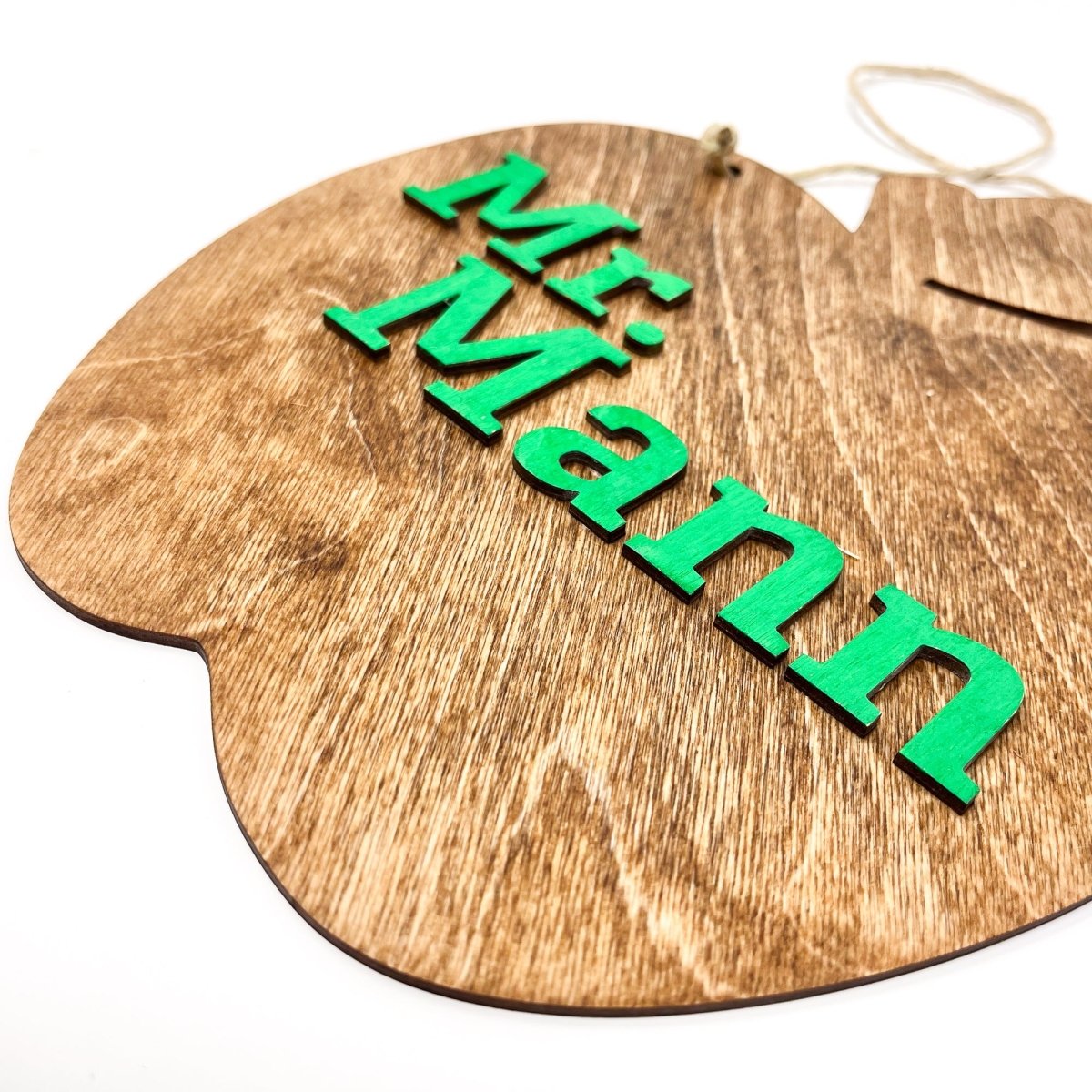 A personalized teacher apple sign made of natural wood, featuring raised lettering and colorful design, ready to hang with jute rope.