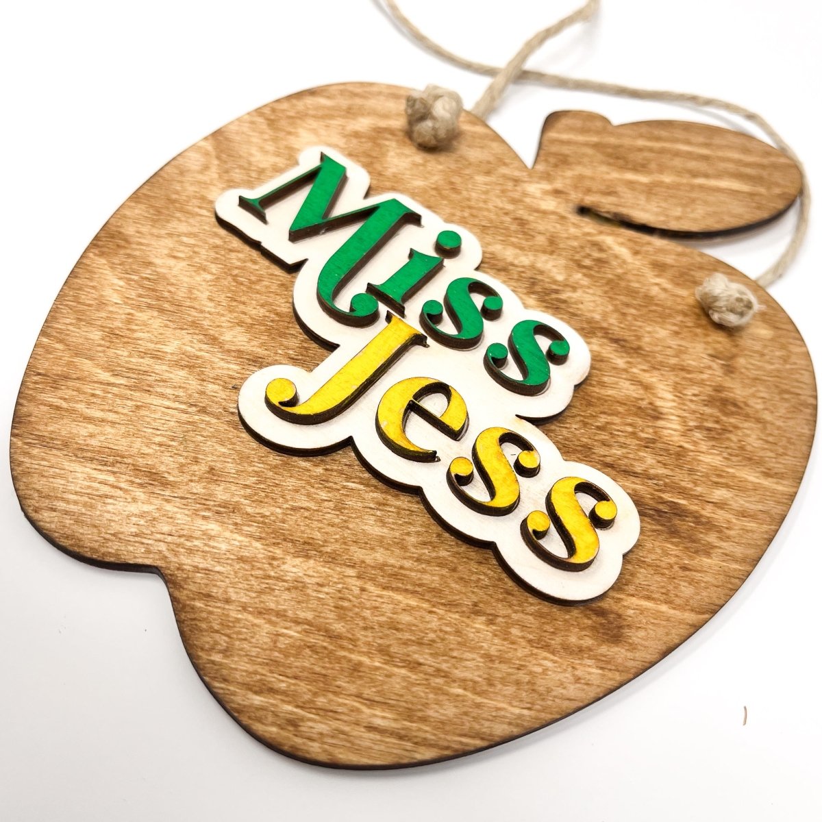 A personalized teacher apple sign made of natural wood, featuring raised lettering and colorful design, ready to hang with jute rope.