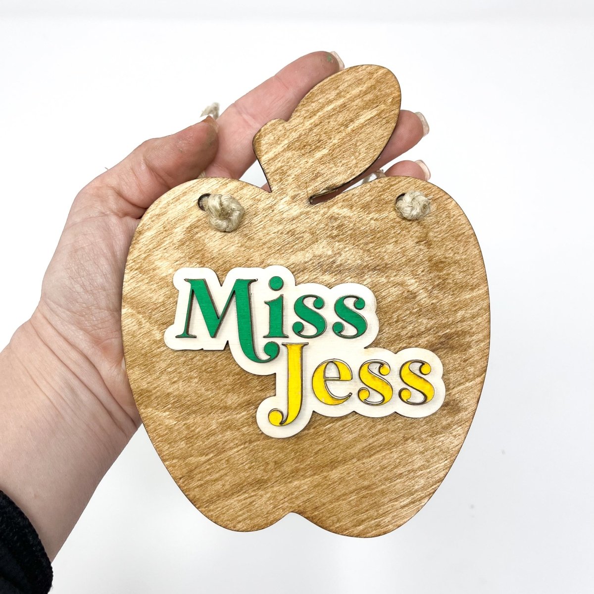 A personalized teacher apple sign made of natural wood, featuring raised lettering and colorful design, ready to hang with jute rope.