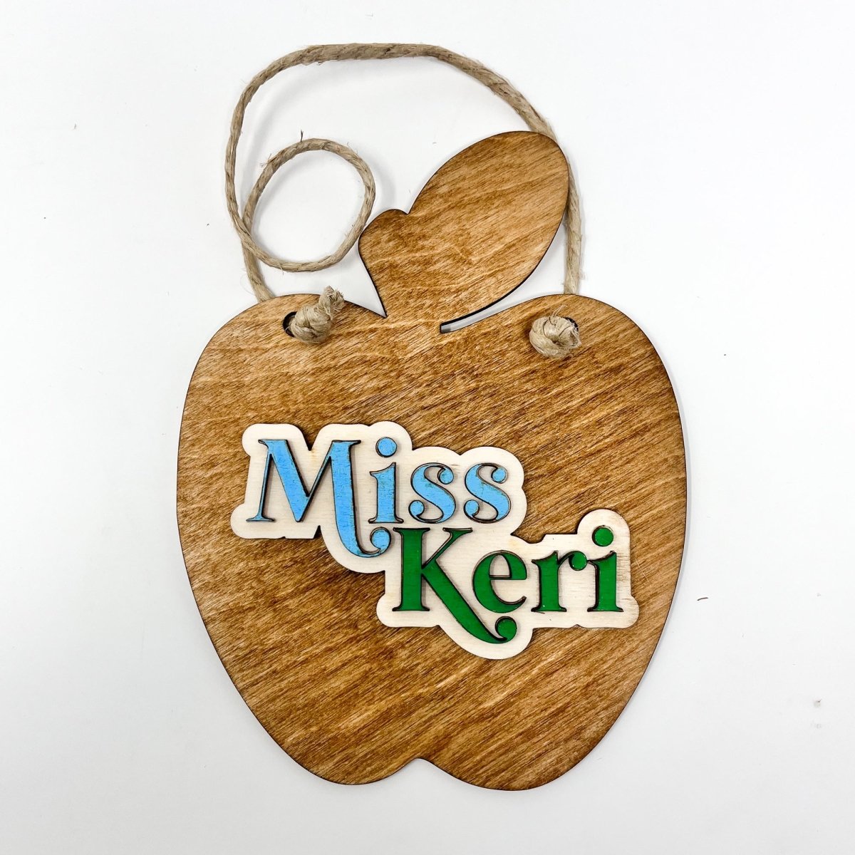 A personalized teacher apple sign made of natural wood, featuring raised lettering and colorful design, ready to hang with jute rope.