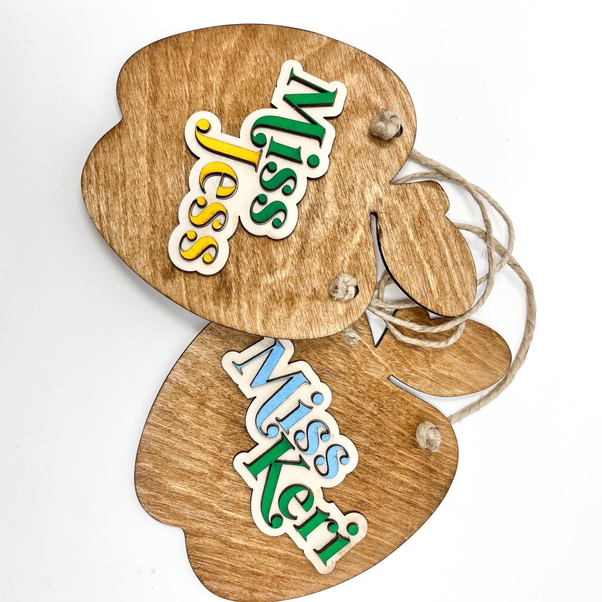 A personalized teacher apple sign made of natural wood, featuring raised lettering and colorful design, ready to hang with jute rope.