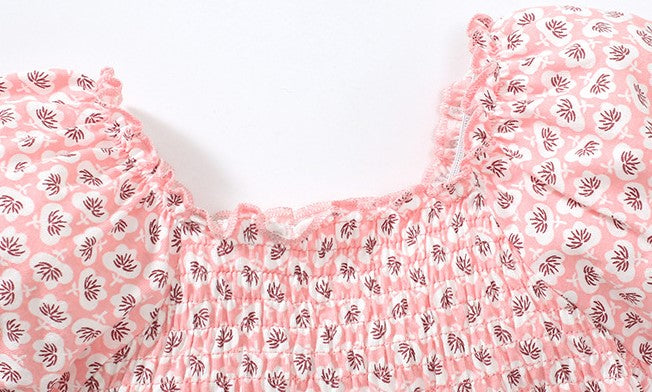 A pink baby girl dress featuring an allover floral graphic design, puff sleeves, and a square neck, made from soft cotton fabric.