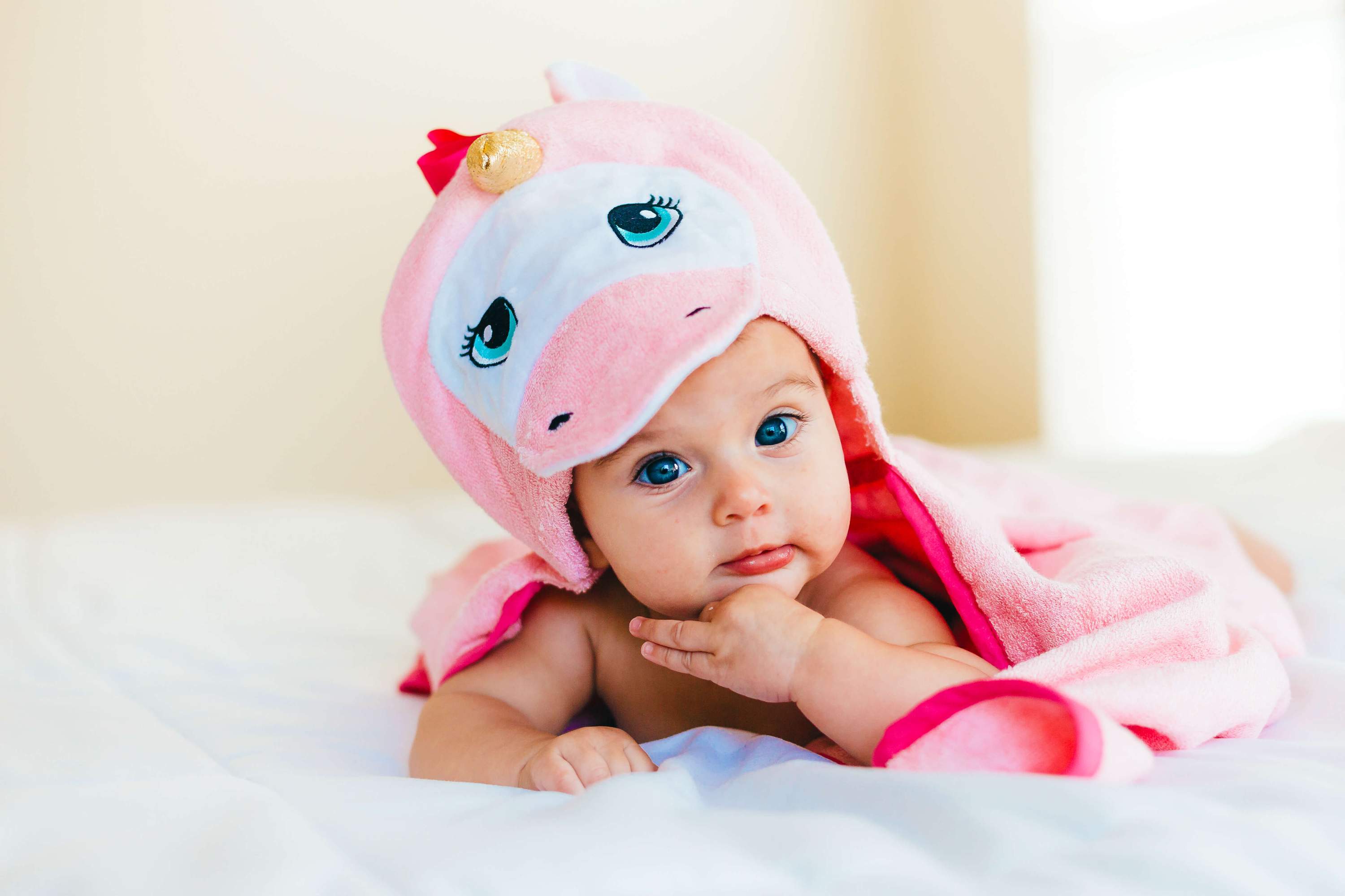 A soft and plush pink unicorn hooded towel designed for babies, featuring a cute unicorn face and ears on the hood.