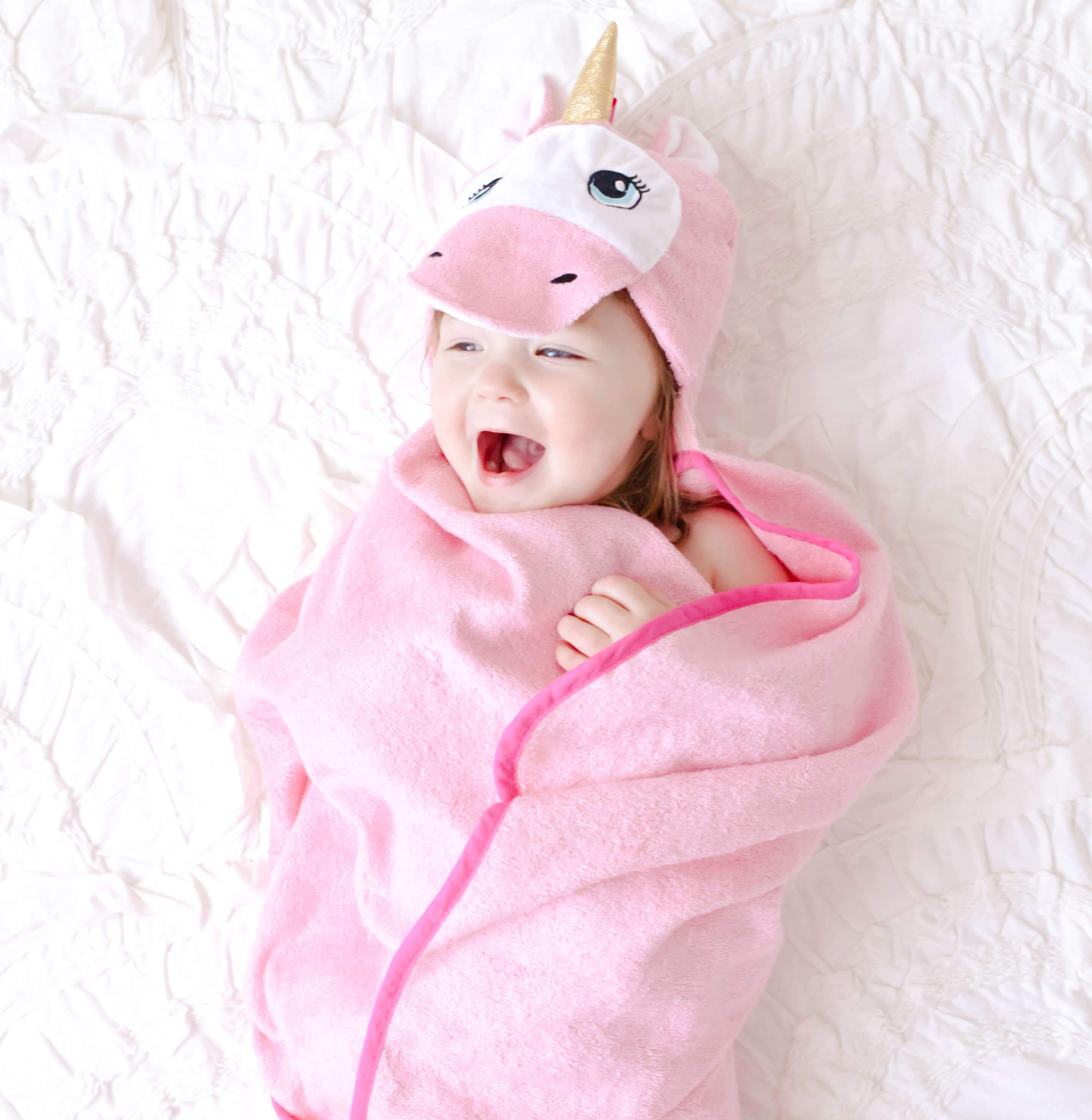 A soft and plush pink unicorn hooded towel designed for babies, featuring a cute unicorn face and ears on the hood.