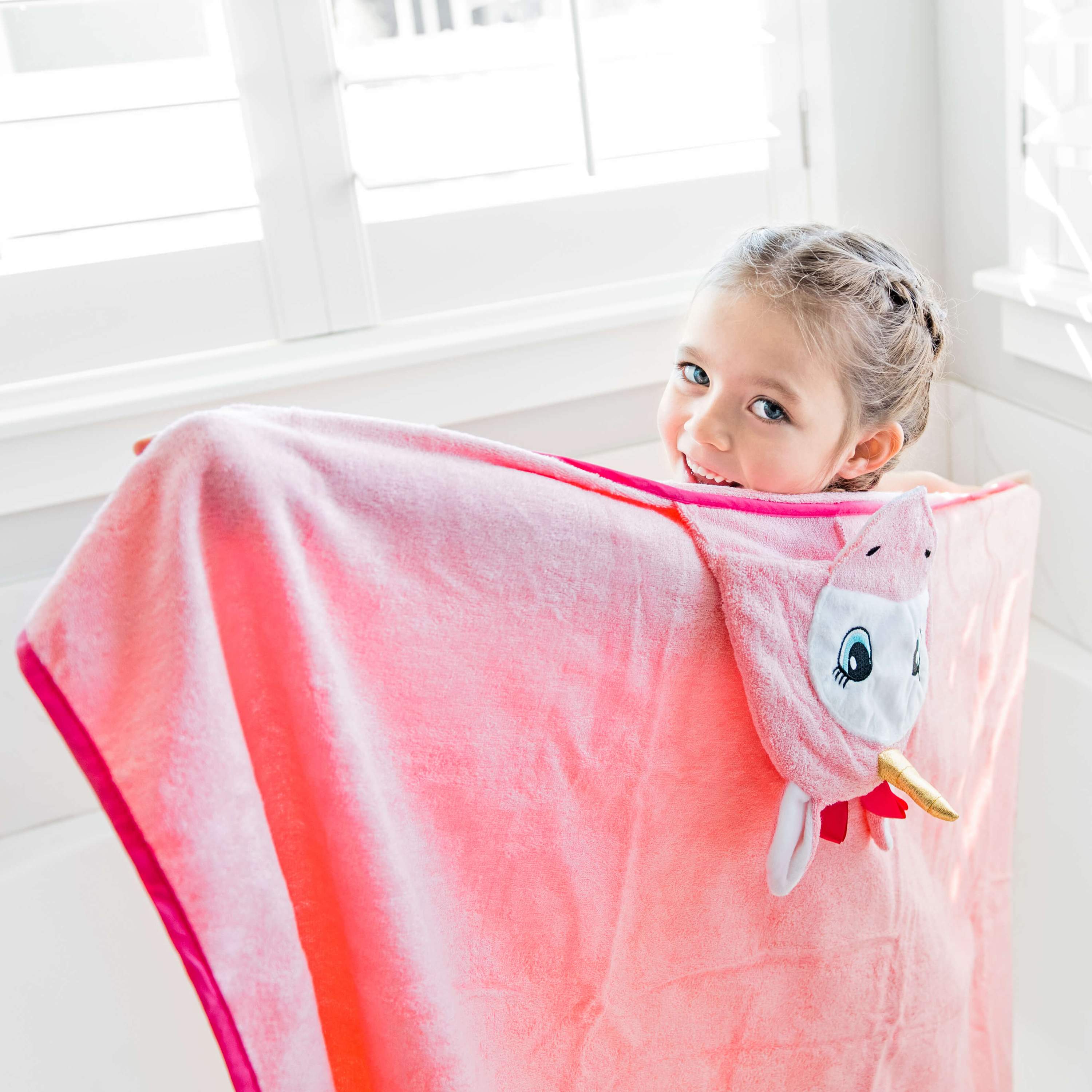 A soft and plush pink unicorn hooded towel designed for babies, featuring a cute unicorn face and ears on the hood.