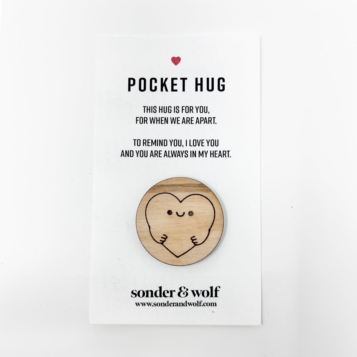 A wooden hug token with an engraved heart, accompanied by a card, symbolizing love and connection.