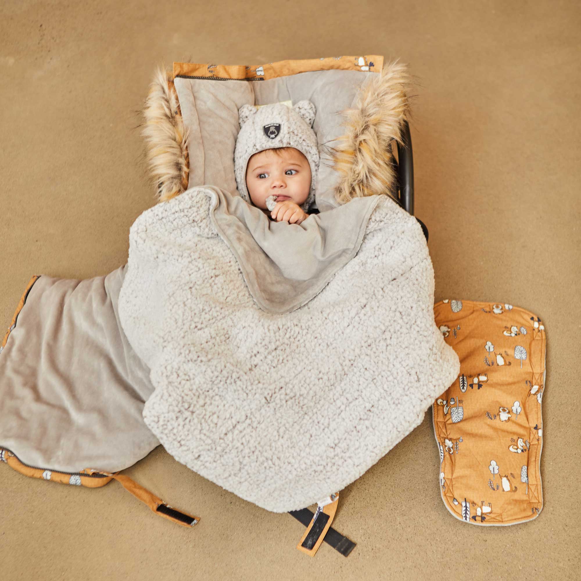 Yellow baby pouch featuring printed woodland animals, insulated design with faux fur trim hood, and included sherpa hat and blanket.