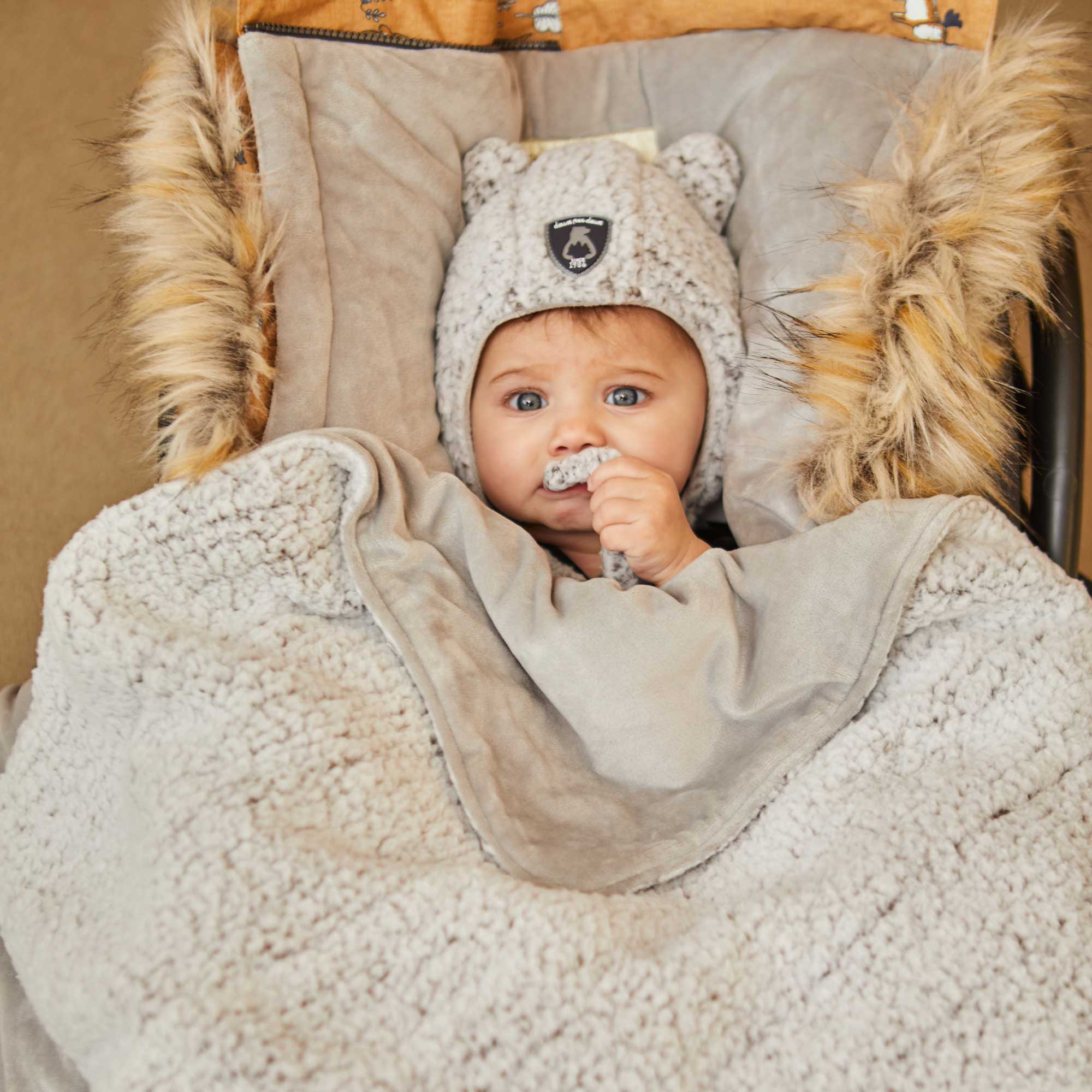 Yellow baby pouch featuring printed woodland animals, insulated design with faux fur trim hood, and included sherpa hat and blanket.