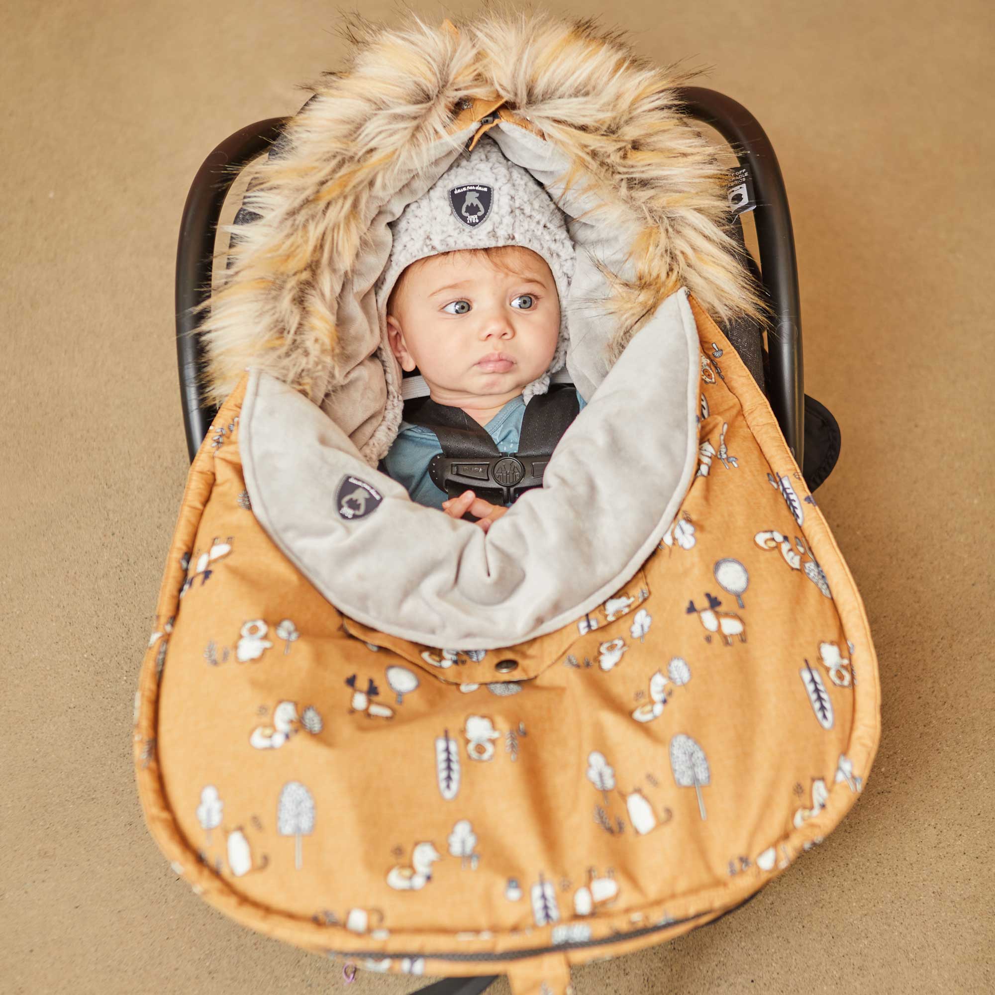 Yellow baby pouch featuring printed woodland animals, insulated design with faux fur trim hood, and included sherpa hat and blanket.