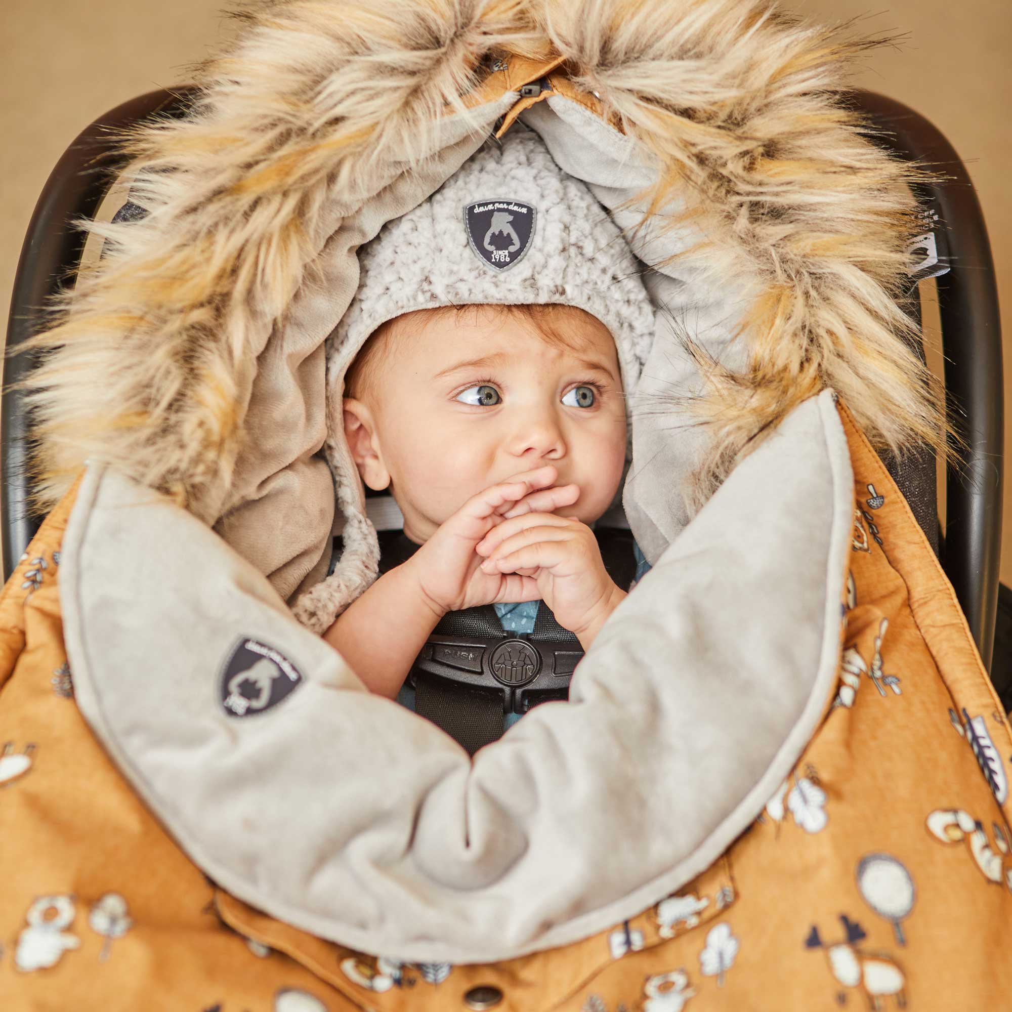 Yellow baby pouch featuring printed woodland animals, insulated design with faux fur trim hood, and included sherpa hat and blanket.