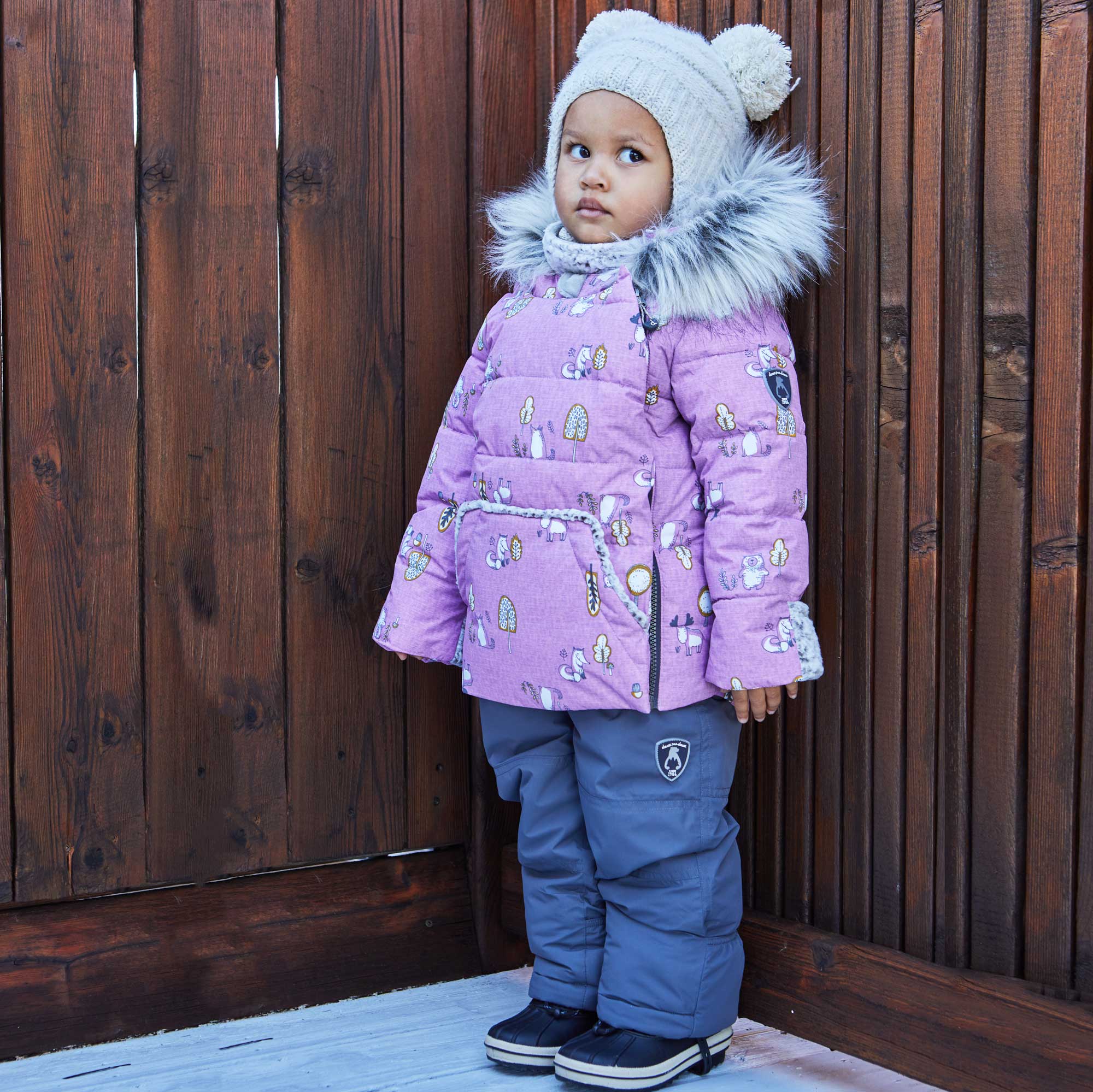 A two-piece baby snowsuit in lilac featuring a woodland animals print, with solid pants and a stylish jacket with faux fur trim.