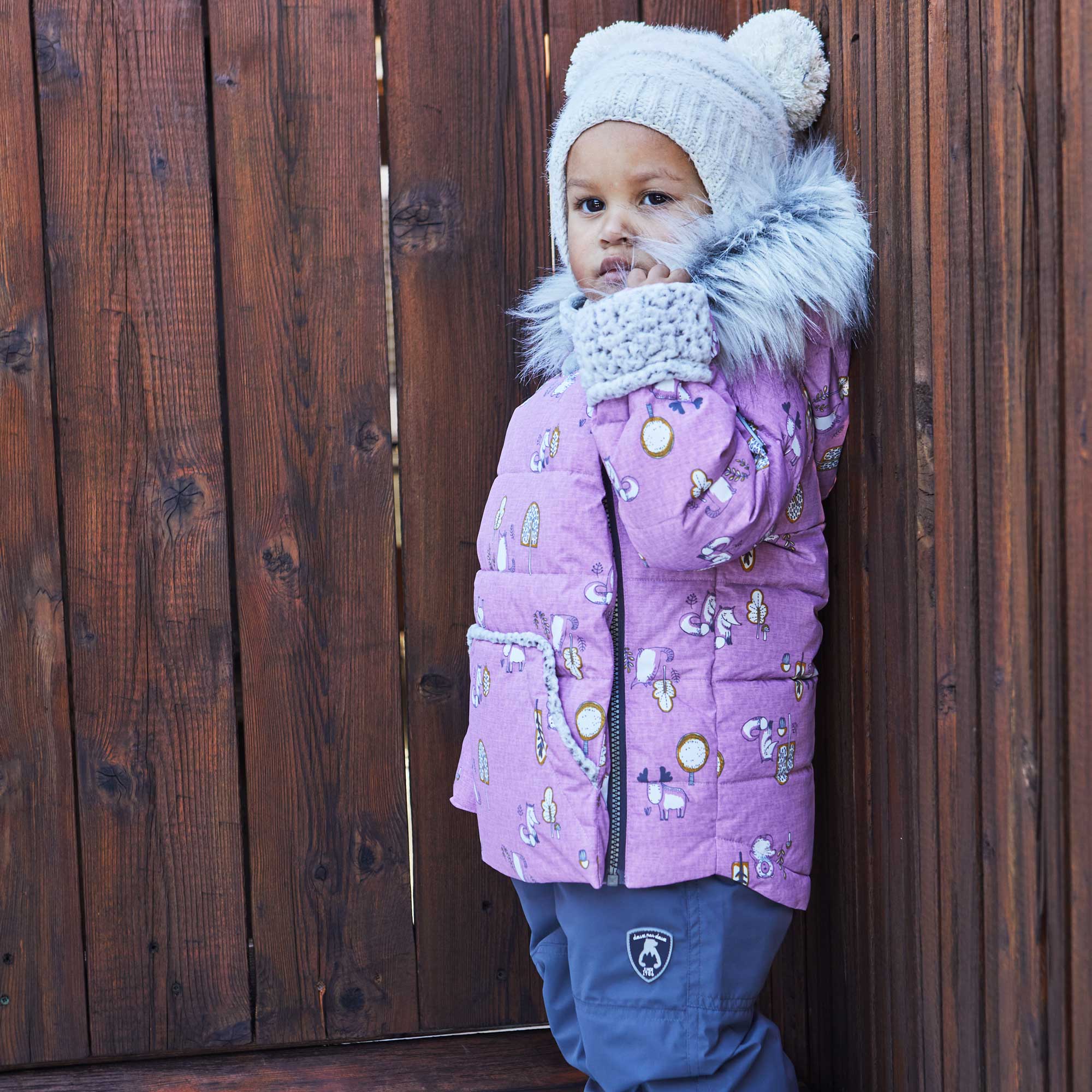 A two-piece baby snowsuit in lilac featuring a woodland animals print, with solid pants and a stylish jacket with faux fur trim.