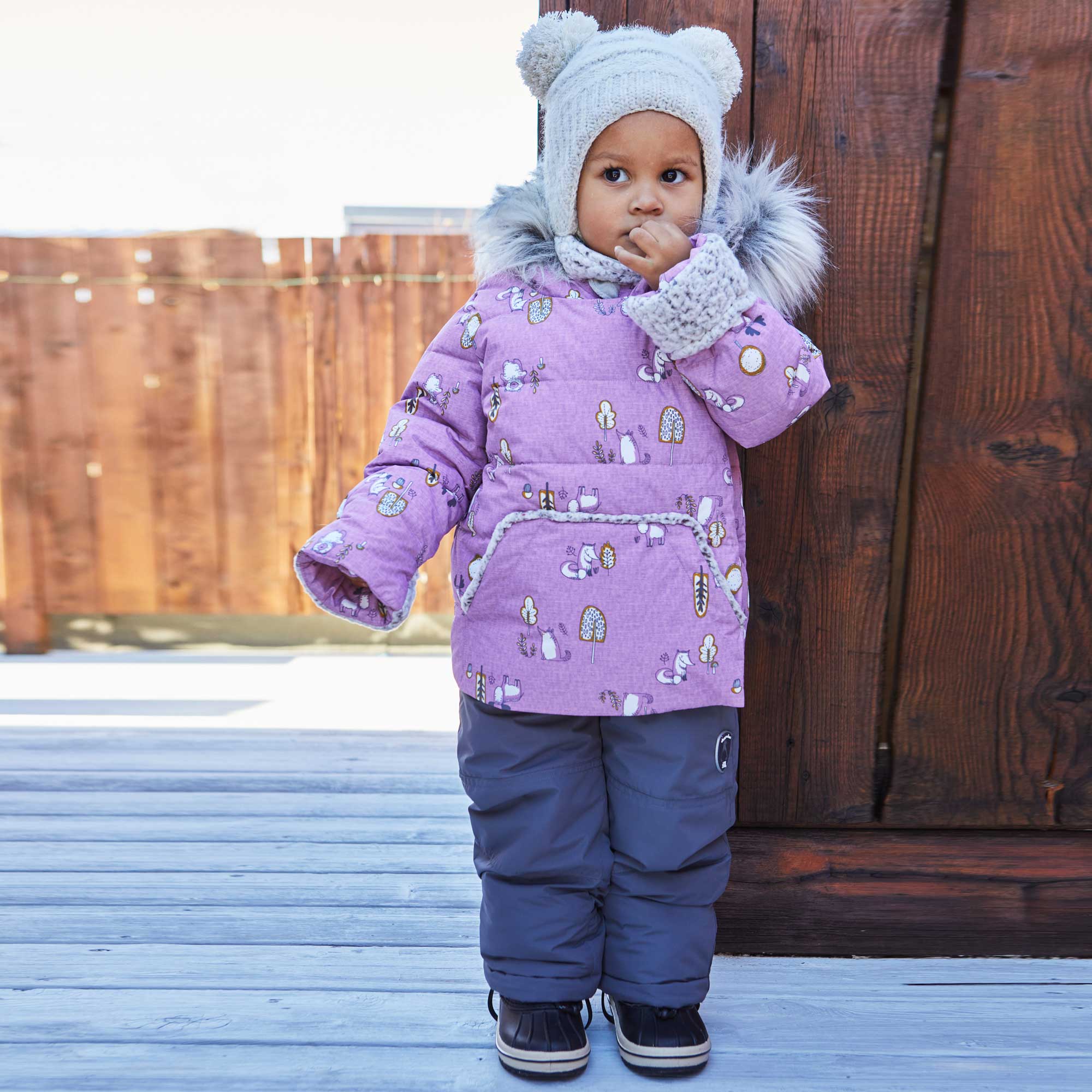 A two-piece baby snowsuit in lilac featuring a woodland animals print, with solid pants and a stylish jacket with faux fur trim.