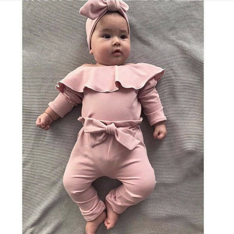 Baby in pink outfit on bed.