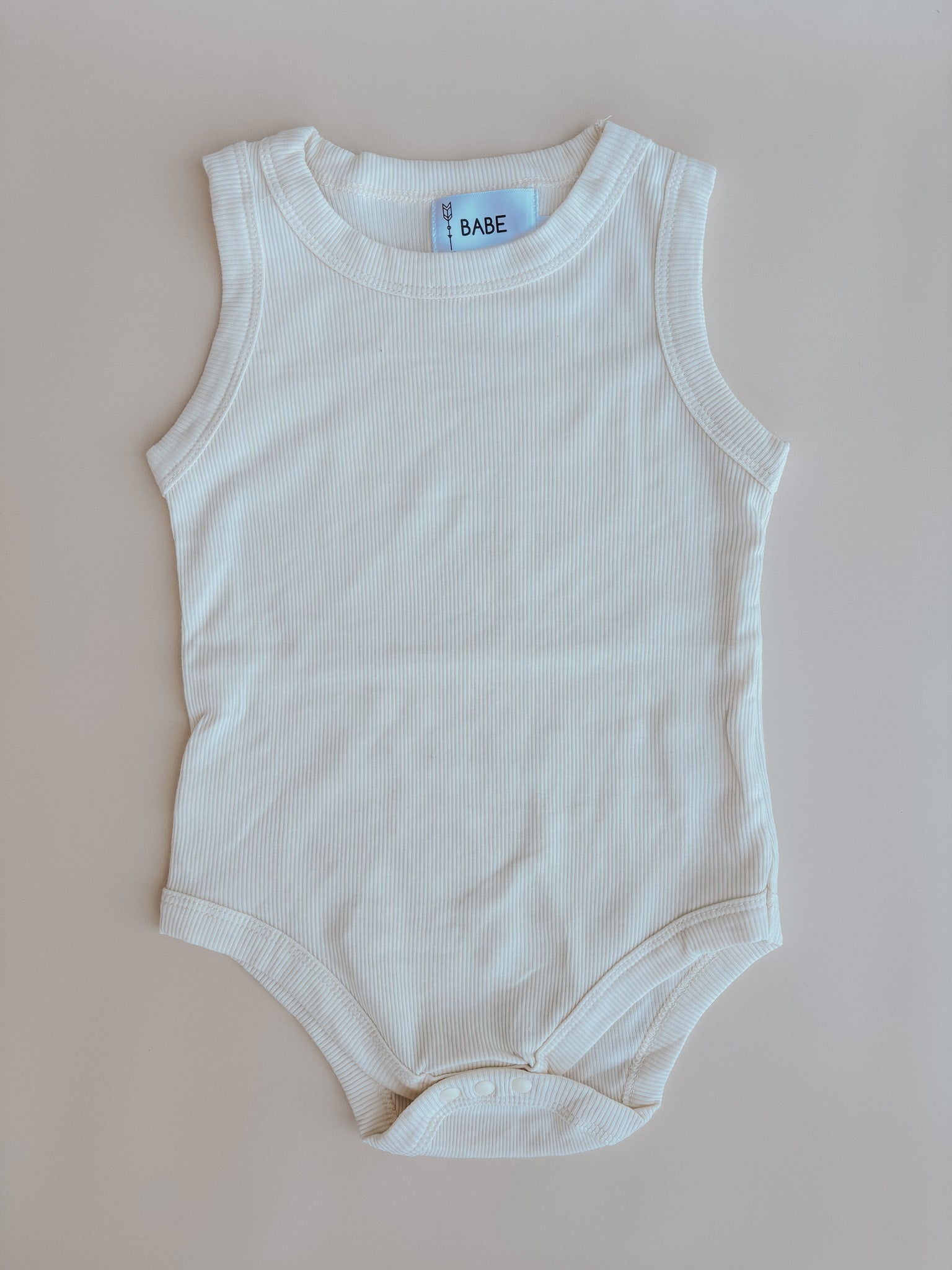 A soft ribbed cotton baby romper in cream and taupe, featuring convenient diaper snaps, perfect for summer outings.