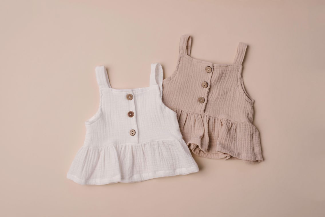 A soft cotton ruffle tank top in beige and white, perfect for layering and comfortable wear for children.