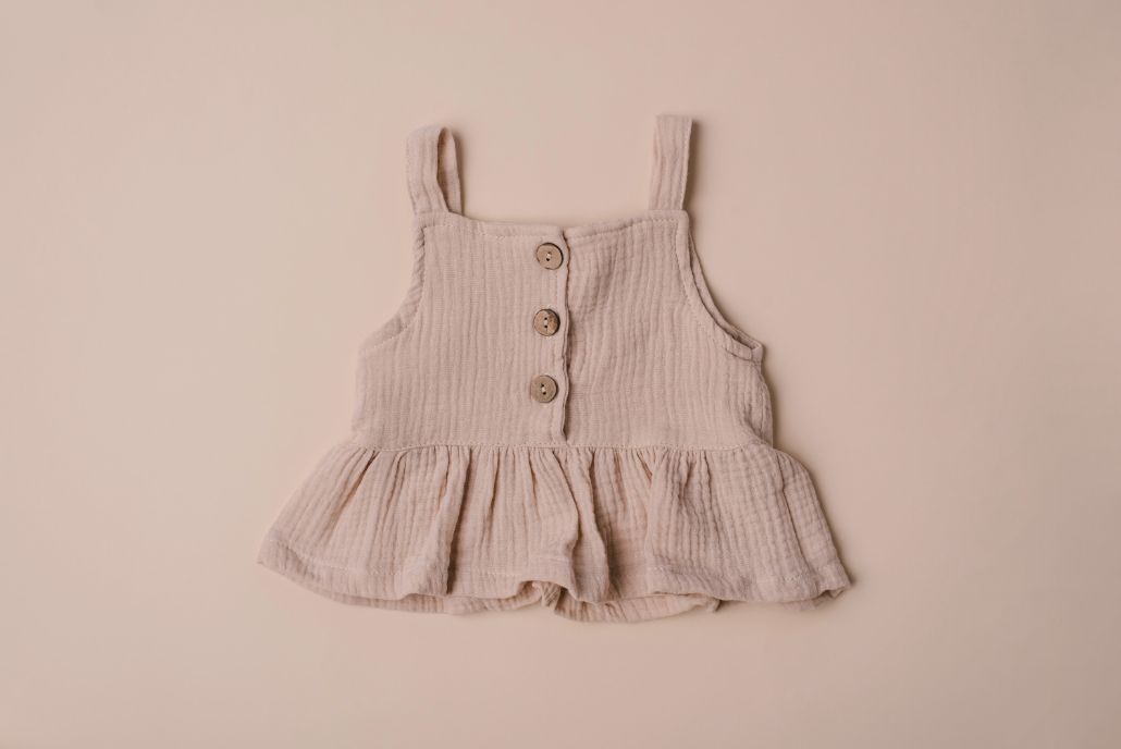 A soft cotton ruffle tank top in beige and white, perfect for layering and comfortable wear for children.