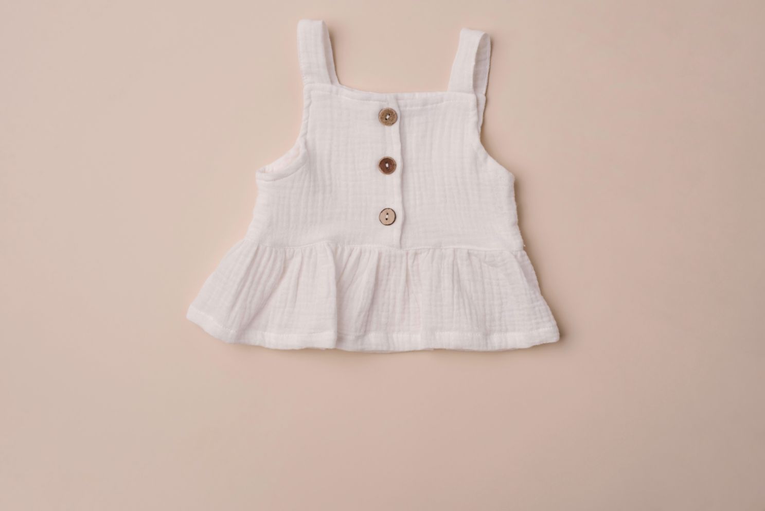 A soft cotton ruffle tank top in beige and white, perfect for layering and comfortable wear for children.