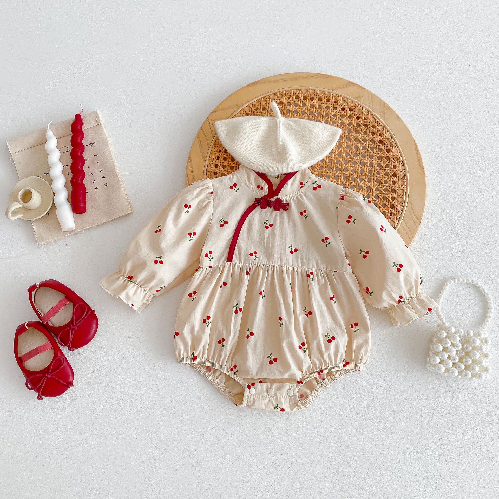 Baby girl wearing a cherry print long sleeves onesie in apricot color, showcasing a cute and stylish design.