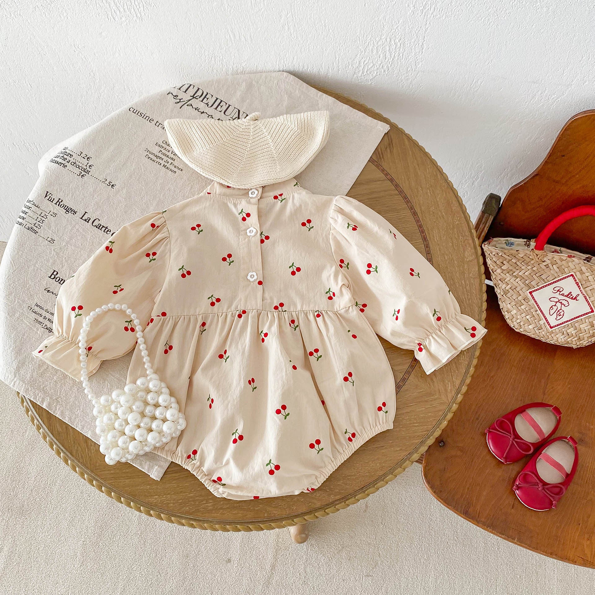 Baby girl wearing a cherry print long sleeves onesie in apricot color, showcasing a cute and stylish design.