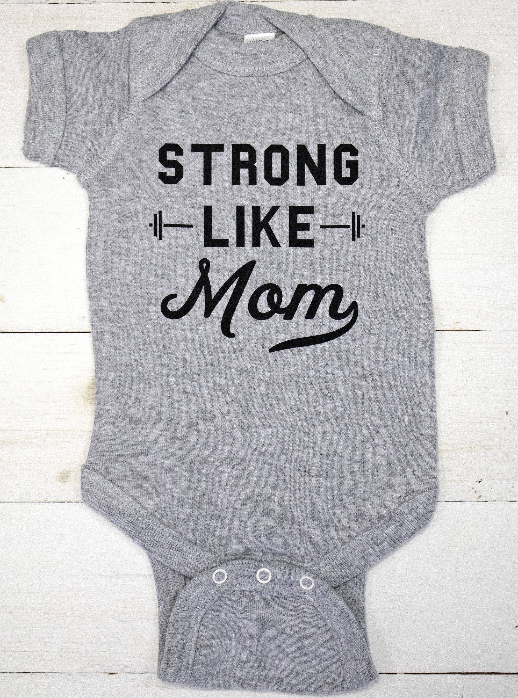 A baby bodysuit featuring the phrase 'Strong Like Mom' in stylish typography, available in Heather Gray, Black, and White colors.