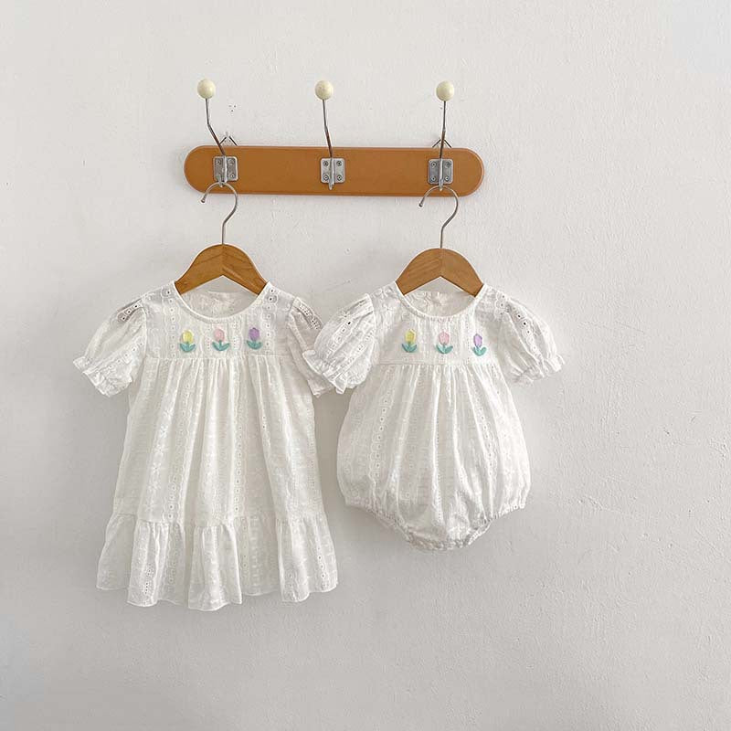 A cute summer dress for baby girls featuring floral embroidery and hollow-out short sleeves, made from soft cotton in white.