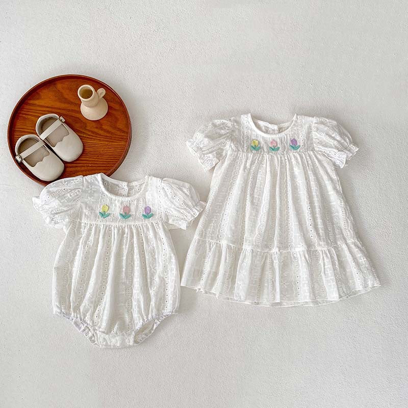 A cute summer dress for baby girls featuring floral embroidery and hollow-out short sleeves, made from soft cotton in white.