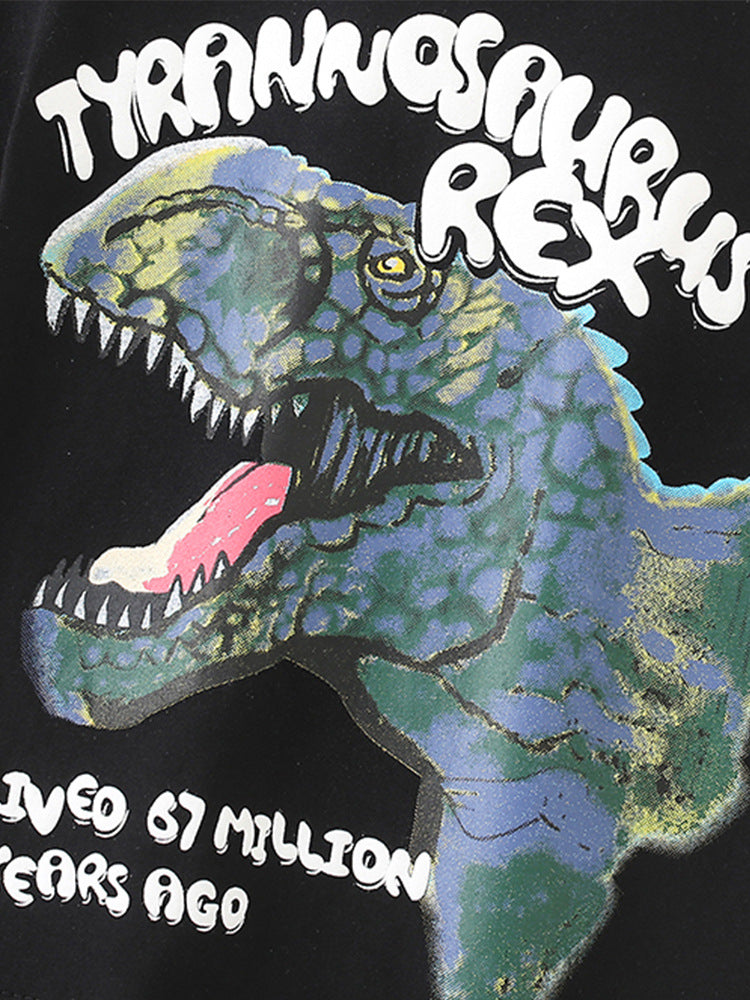 A black short-sleeved t-shirt featuring a fierce cartoon dinosaur print, designed for boys aged 12 months to 10 years.