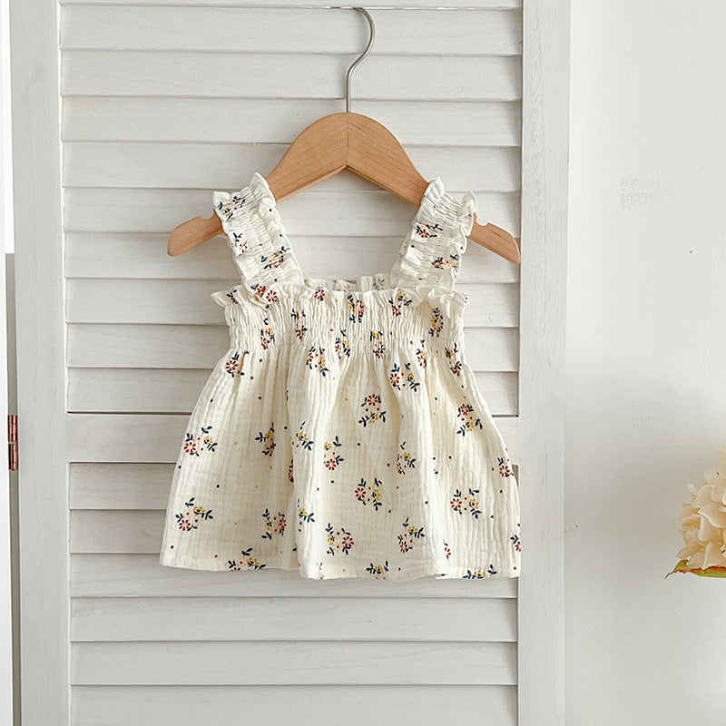 A cute baby girl wearing a sleeveless floral pattern strap top, showcasing vibrant flowers against a white background.