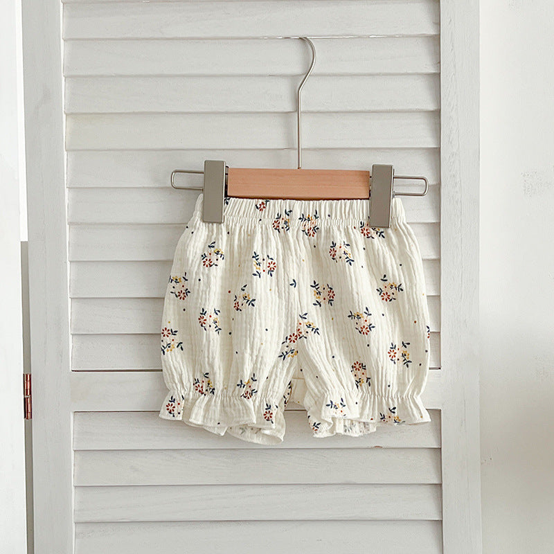 A cute baby girl wearing a sleeveless floral pattern strap top, showcasing vibrant flowers against a white background.