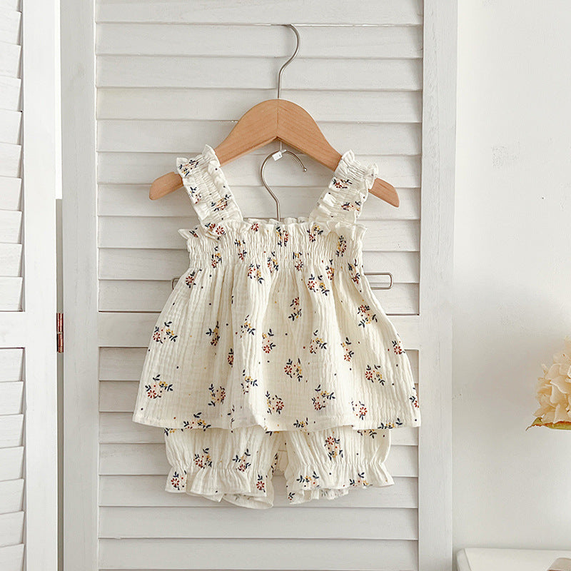 A cute baby girl wearing a sleeveless floral pattern strap top, showcasing vibrant flowers against a white background.