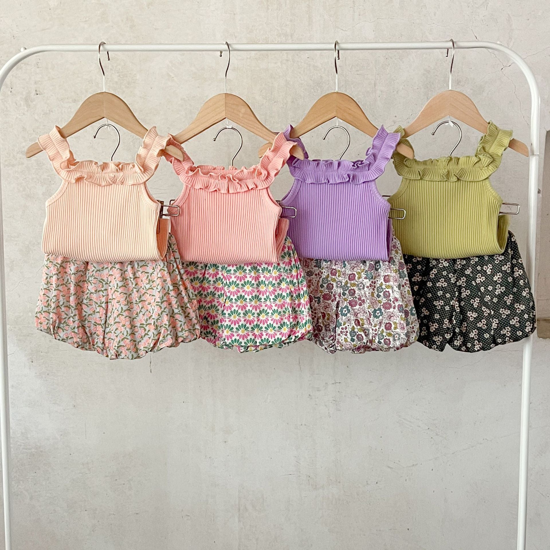 A collection of baby girls' sleeveless solid color strap tops in pink, purple, green, and beige, made from soft cotton fabric.