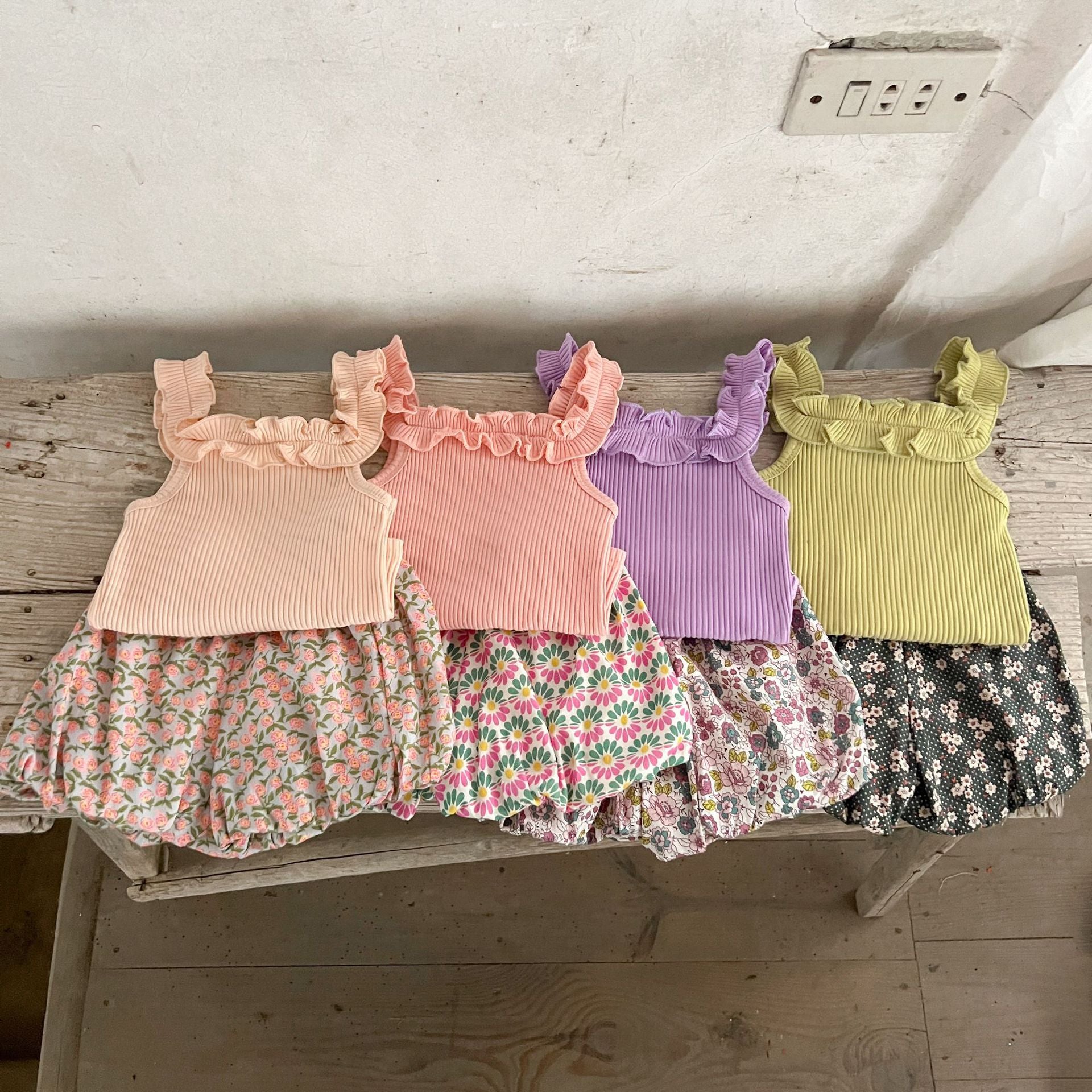 A collection of baby girls' sleeveless solid color strap tops in pink, purple, green, and beige, made from soft cotton fabric.