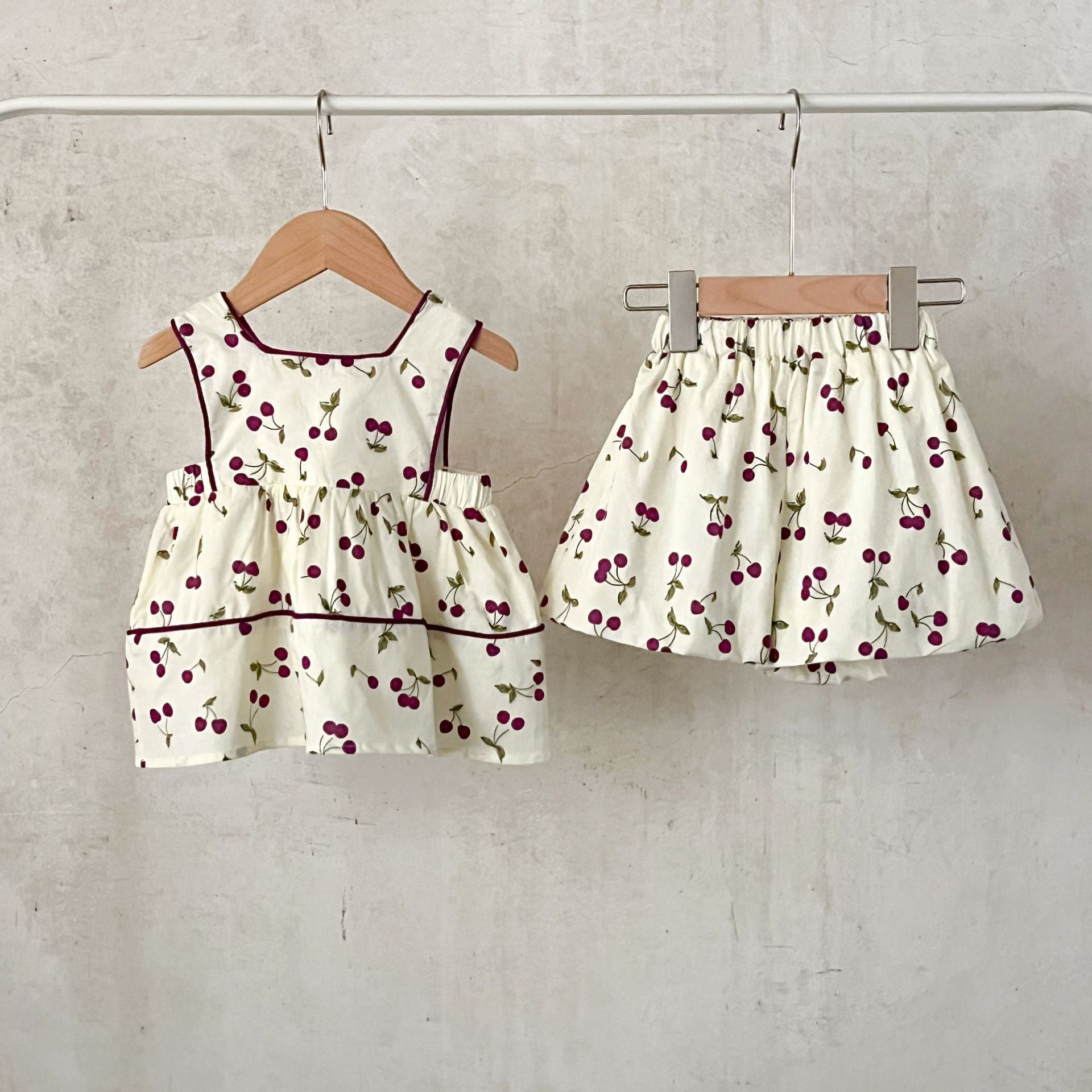 A cute beige sleeveless dress for baby girls featuring a sweet cherry print, perfect for summer wear.