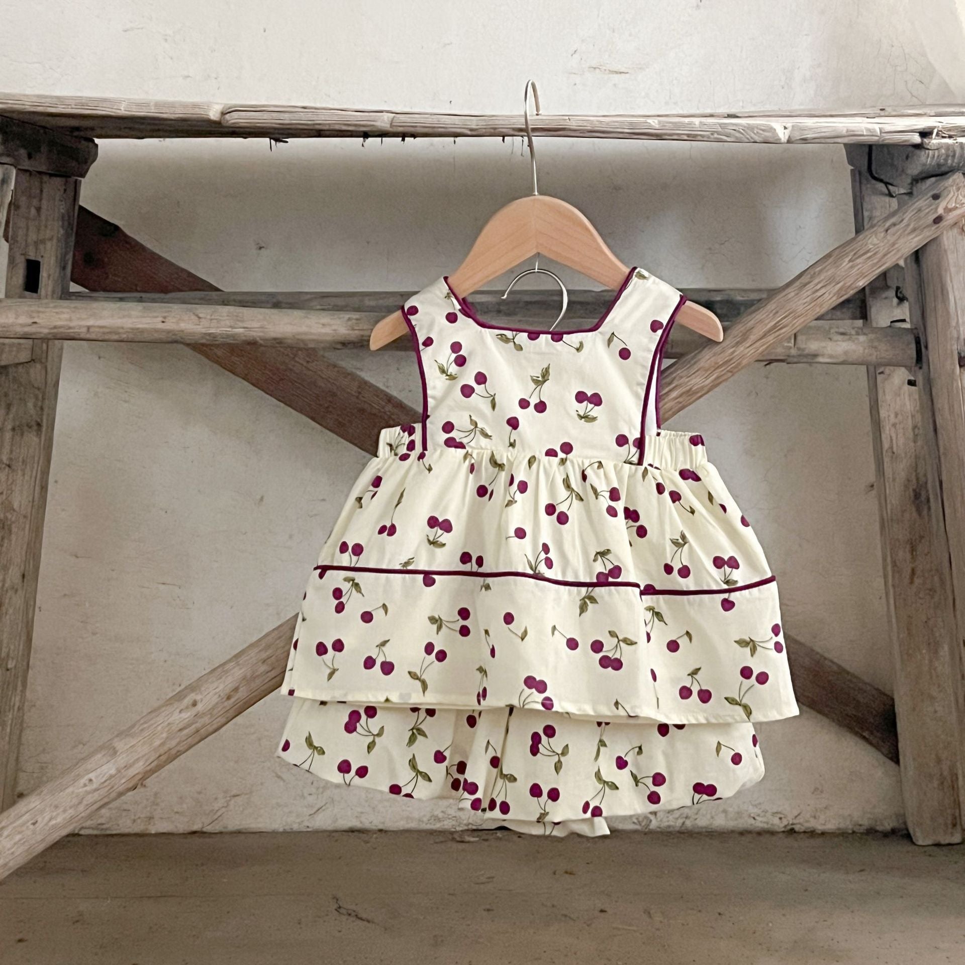 A cute beige sleeveless dress for baby girls featuring a sweet cherry print, perfect for summer wear.