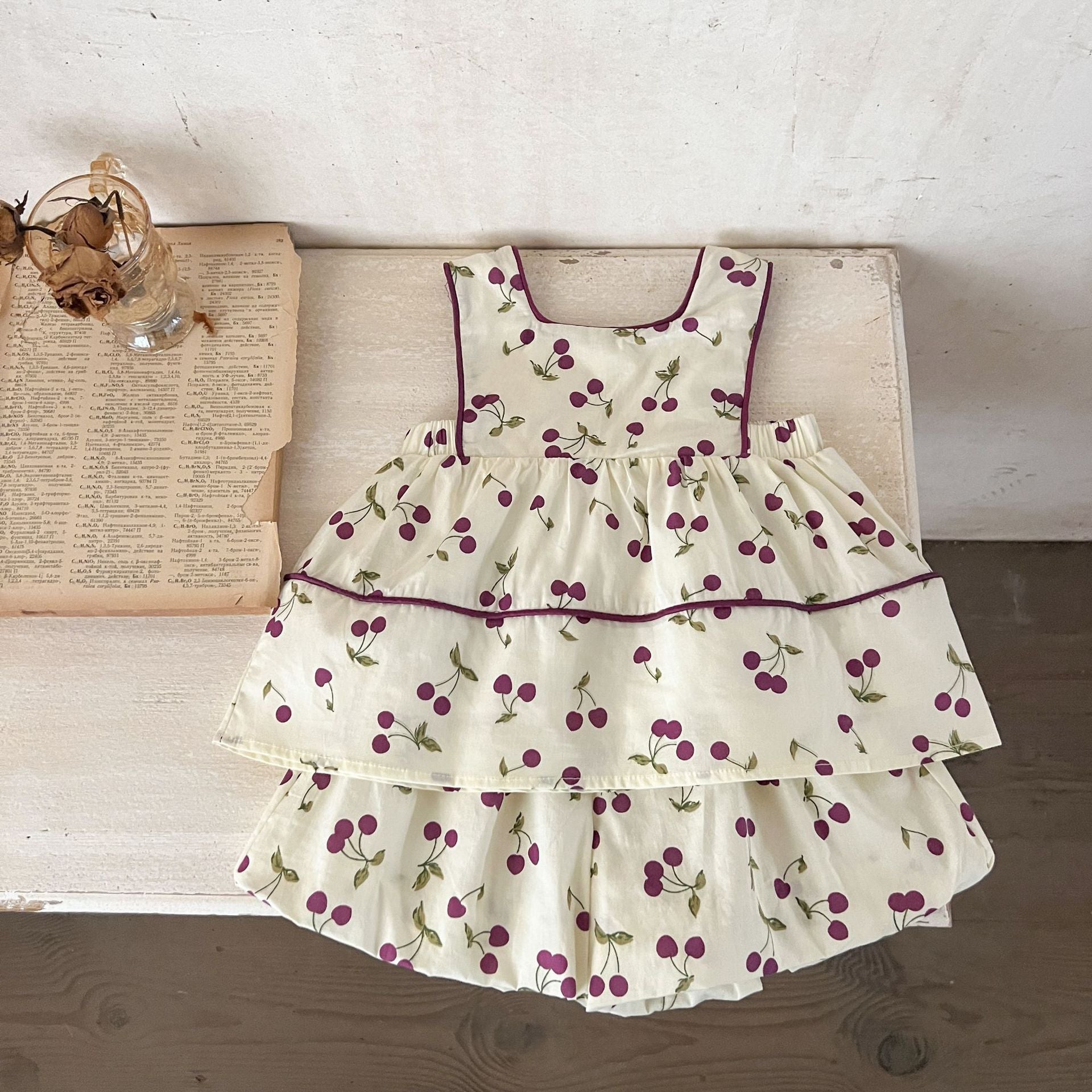 A cute beige sleeveless dress for baby girls featuring a sweet cherry print, perfect for summer wear.