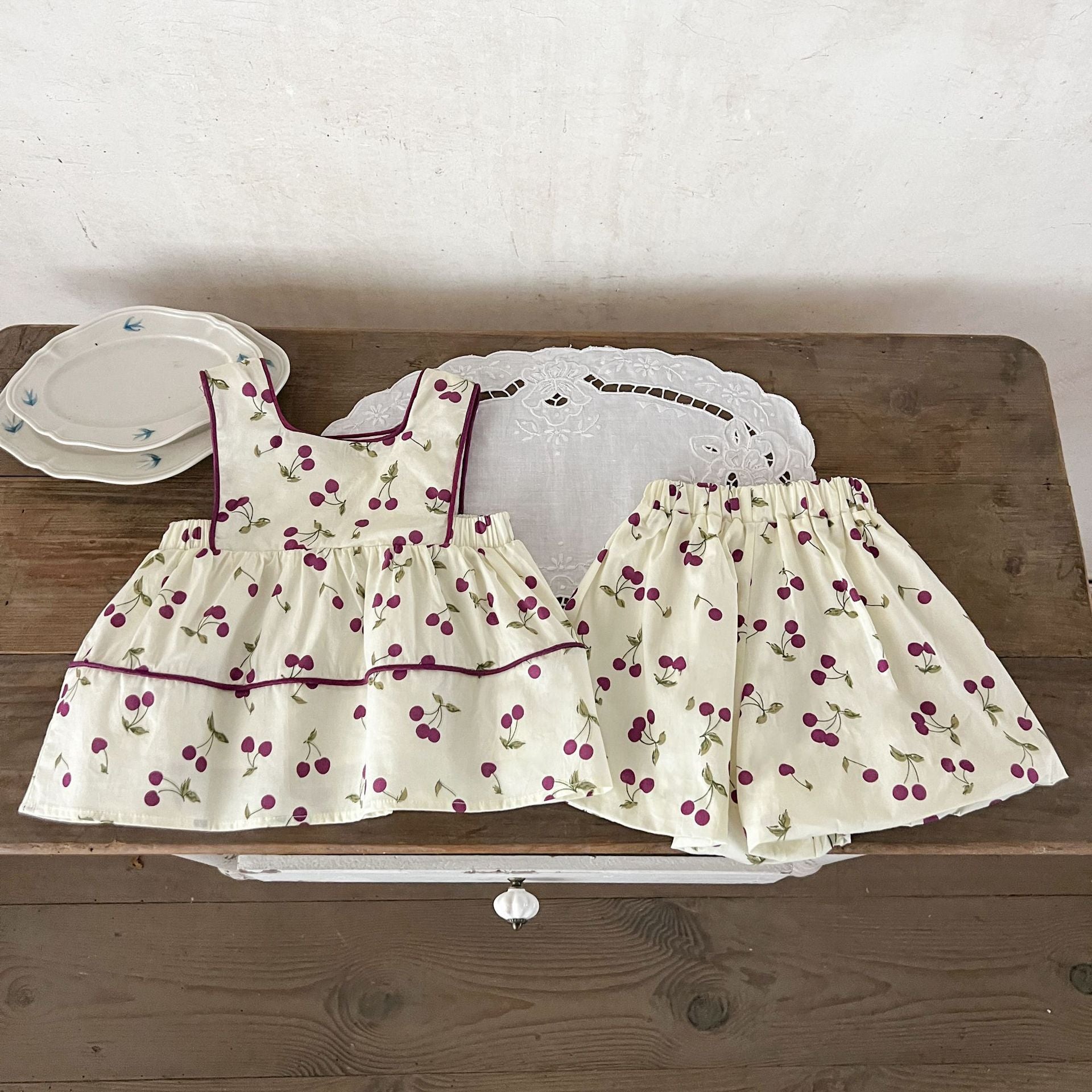 A cute beige sleeveless dress for baby girls featuring a sweet cherry print, perfect for summer wear.