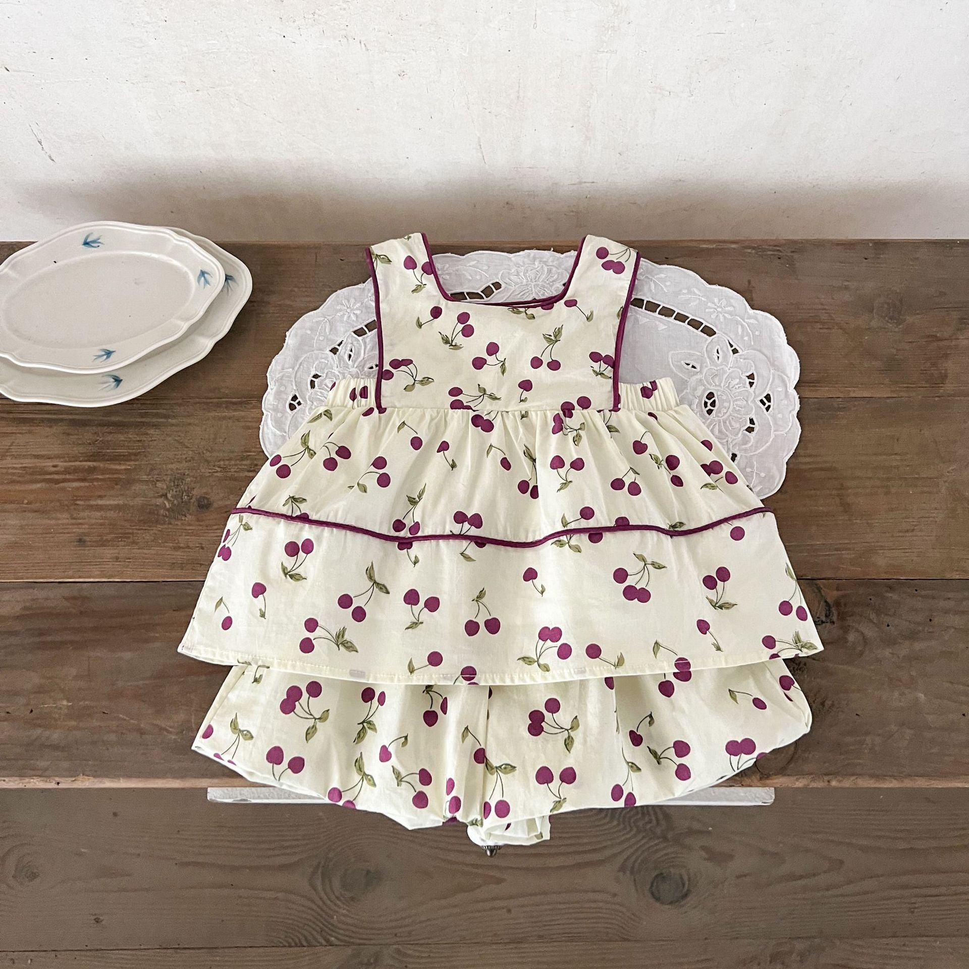 A cute beige sleeveless dress for baby girls featuring a sweet cherry print, perfect for summer wear.