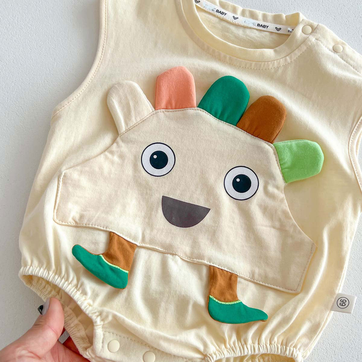 A beige sleeveless crew neck top for babies, made of thin cotton with a cartoon pattern, suitable for summer wear.