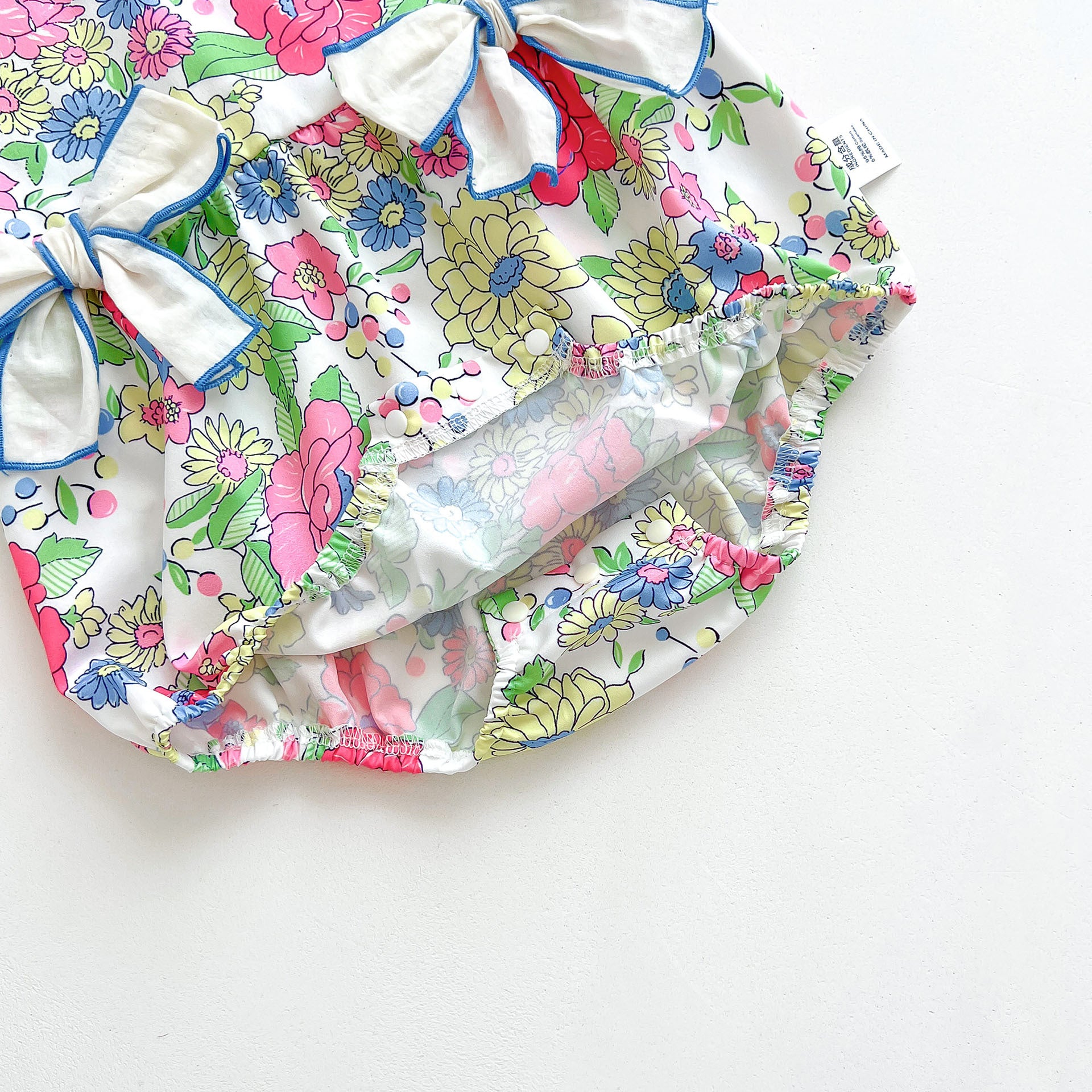 Baby girl wearing a blue floral dress with fly sleeves and 3D bows, perfect for summer.